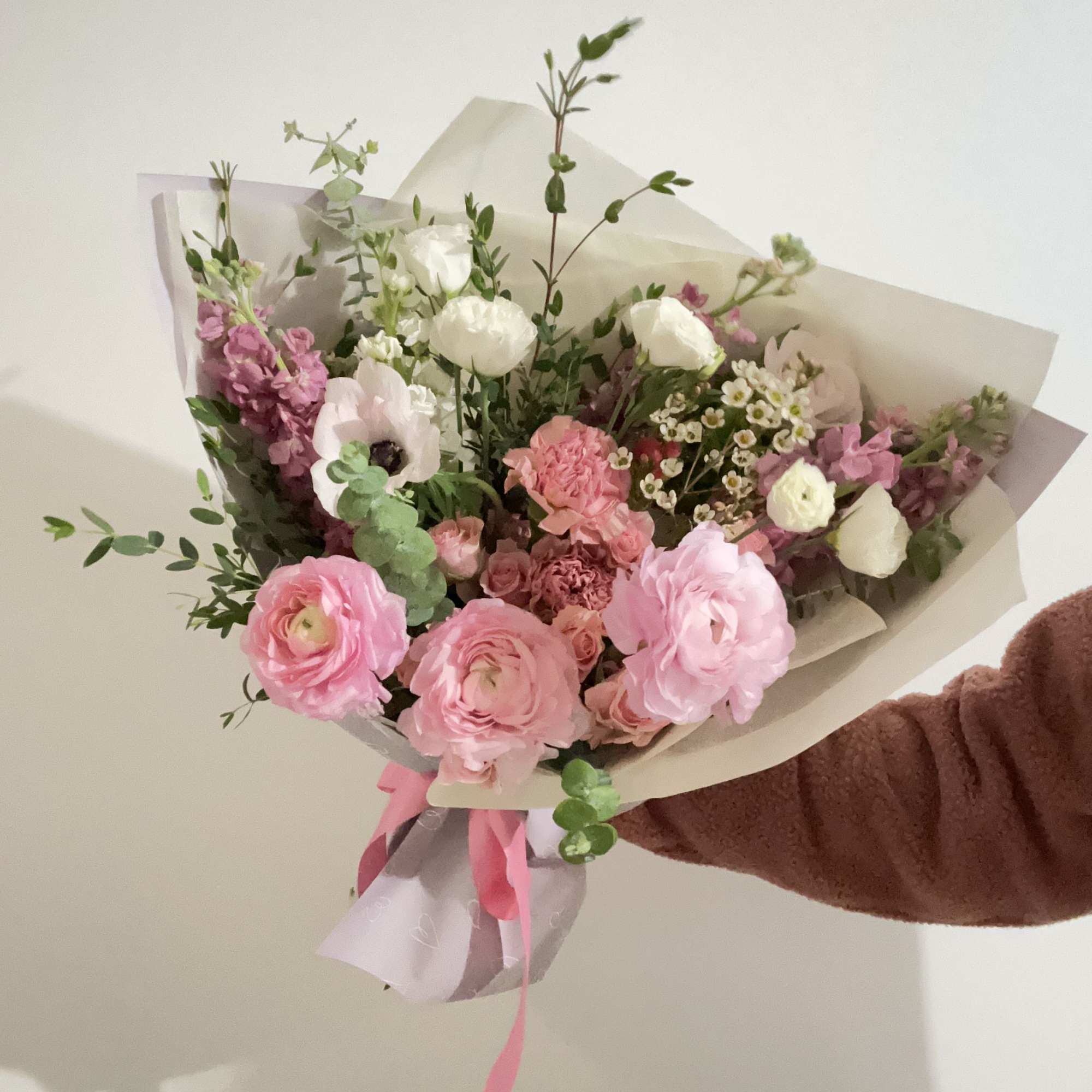 Handheld bouquet of pink and white flowers wrapped in paper