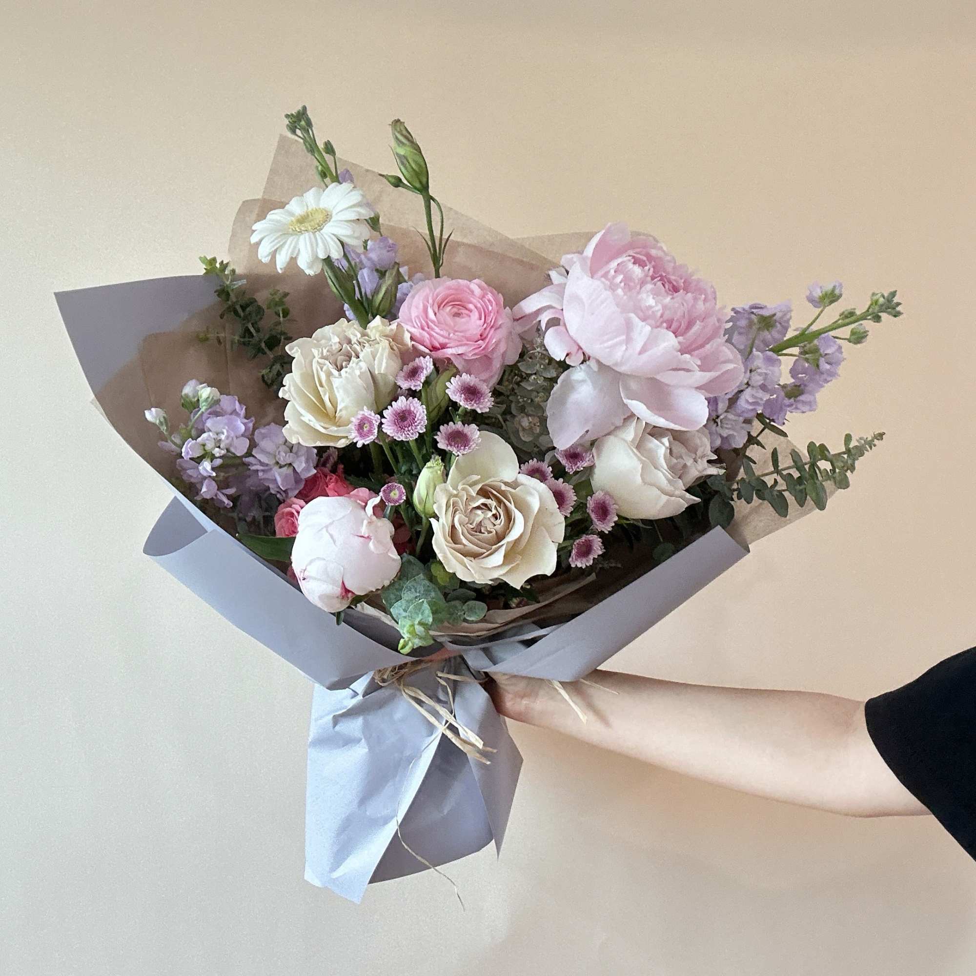 Hand-tied bouquet of pink, white, and lavender flowers wrapped in paper