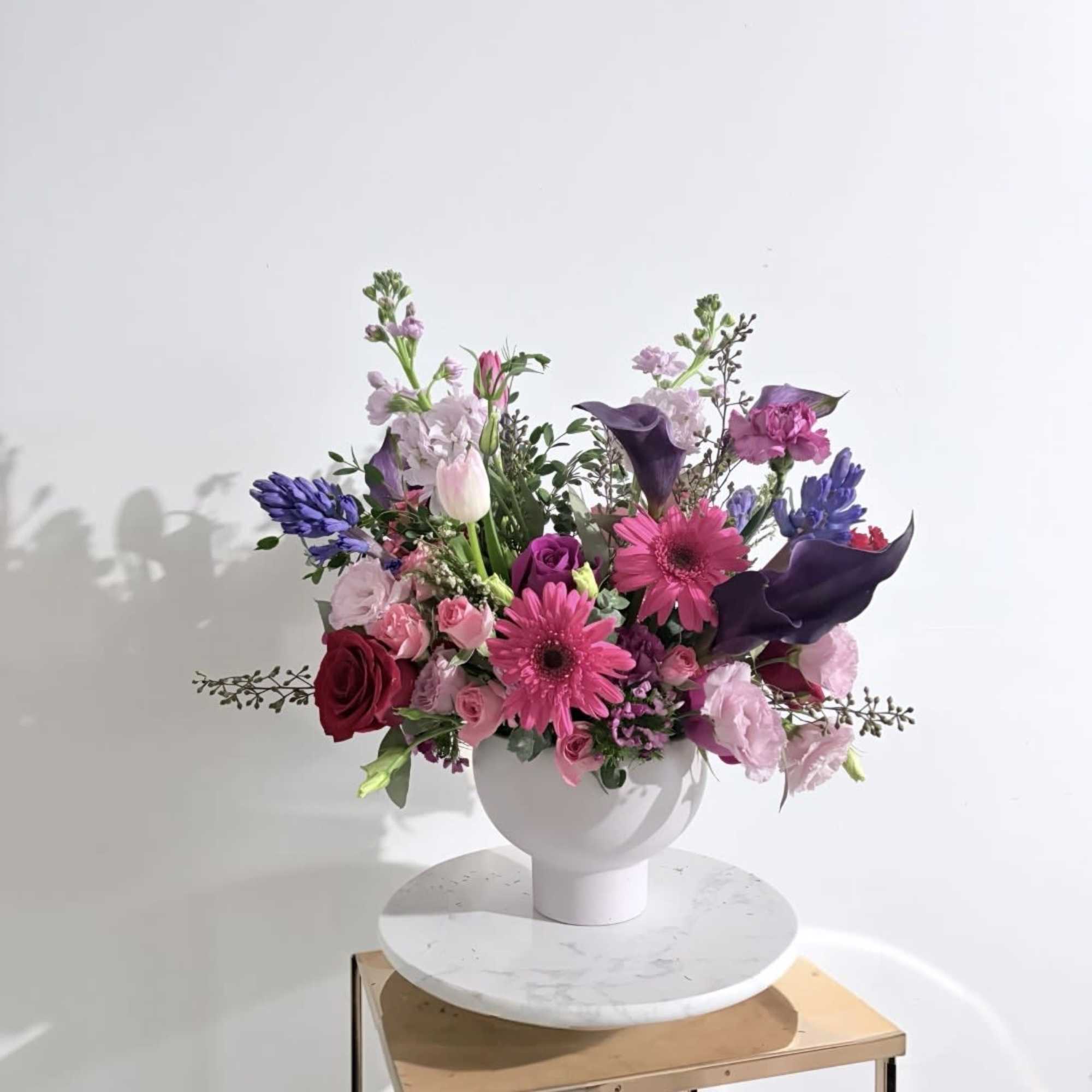 Mixed pink, purple, and white flowers arranged in a white vase