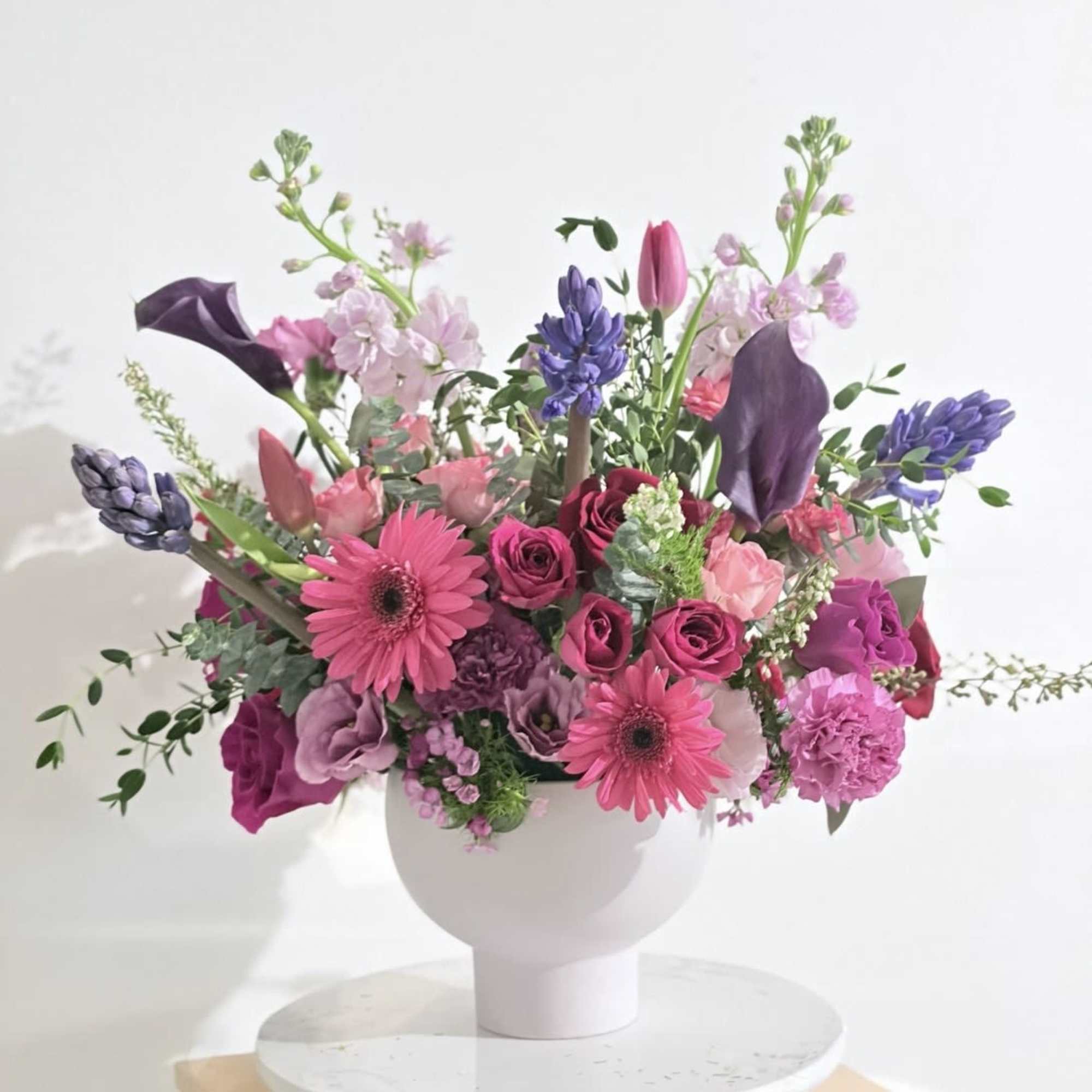 Pink and purple mixed flower arrangement in a white vase