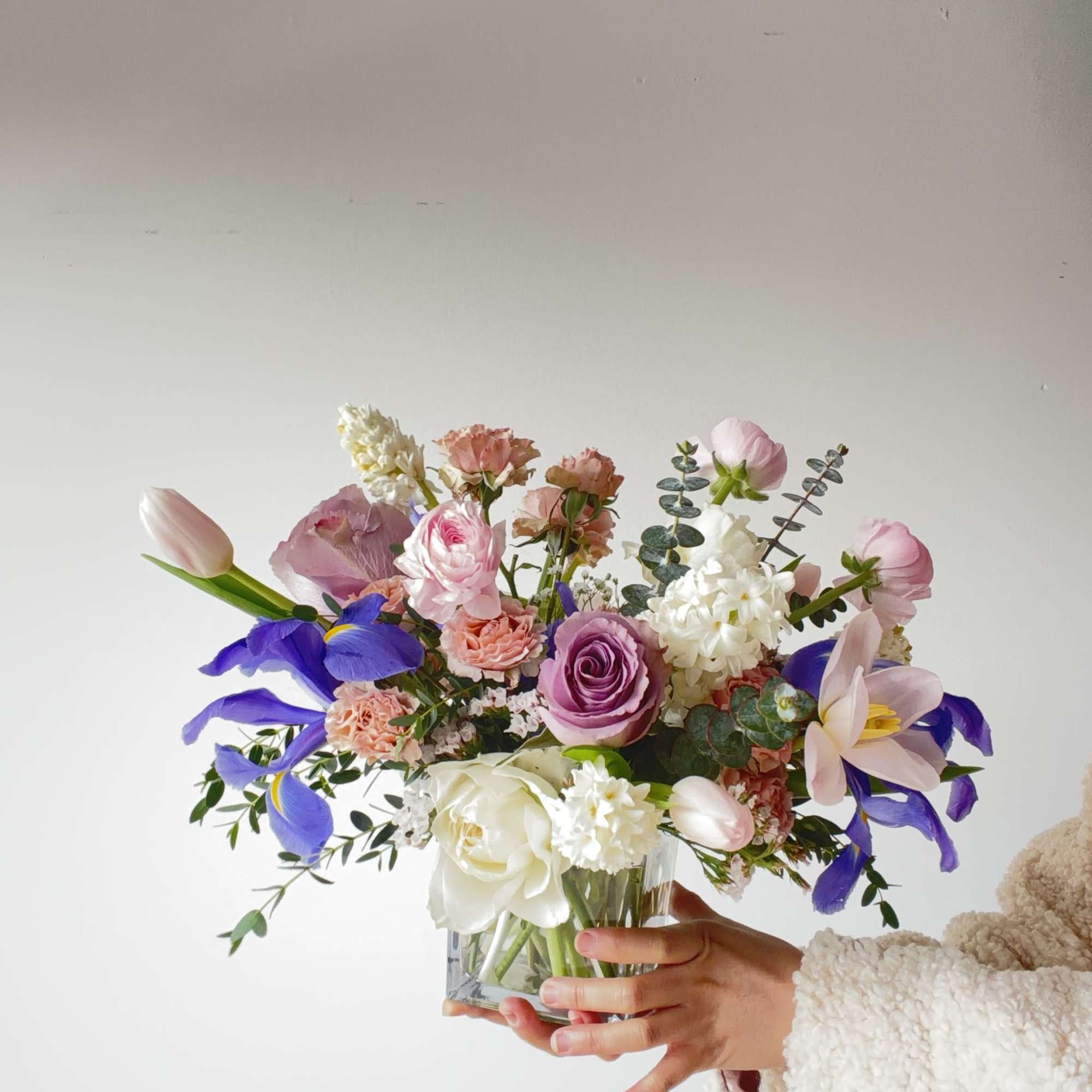 Mixed pastel bouquet in a clear glass vase held by a person