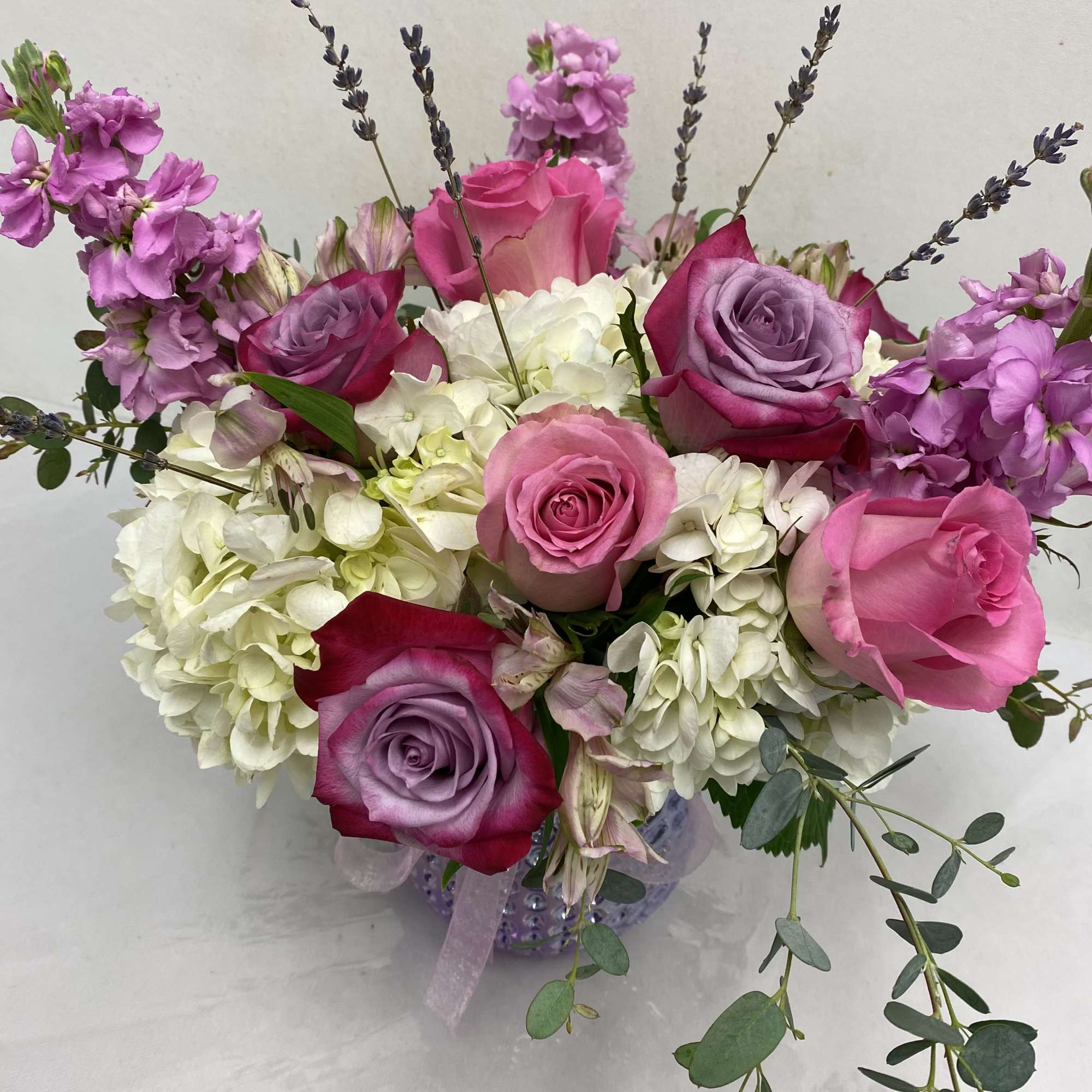 Low round arrangement of pink and lavender roses with white hydrangeas in a glass vase