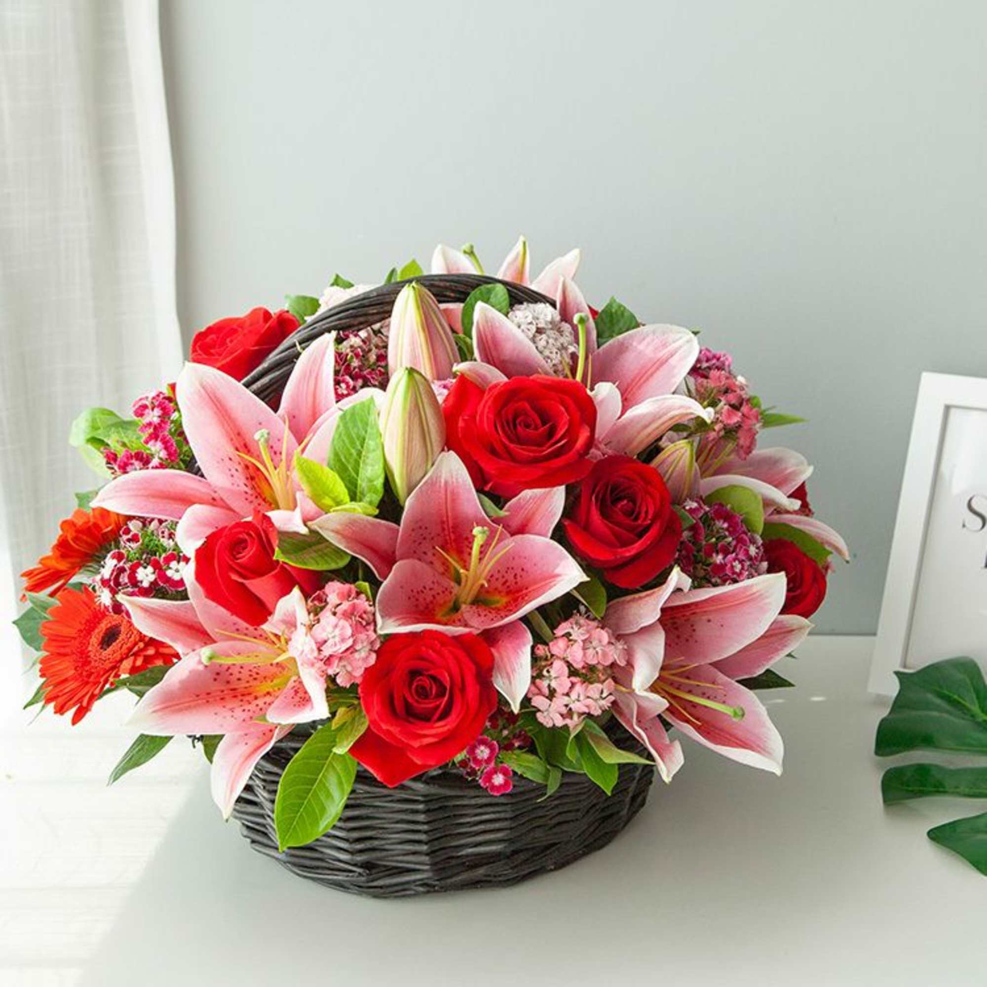 Basket arrangement of pink lilies and red roses