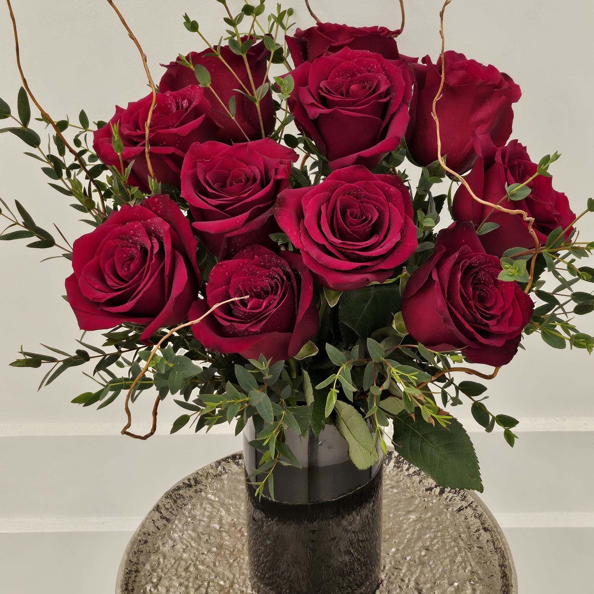 Bouquet of deep red roses in a dark vase with greenery