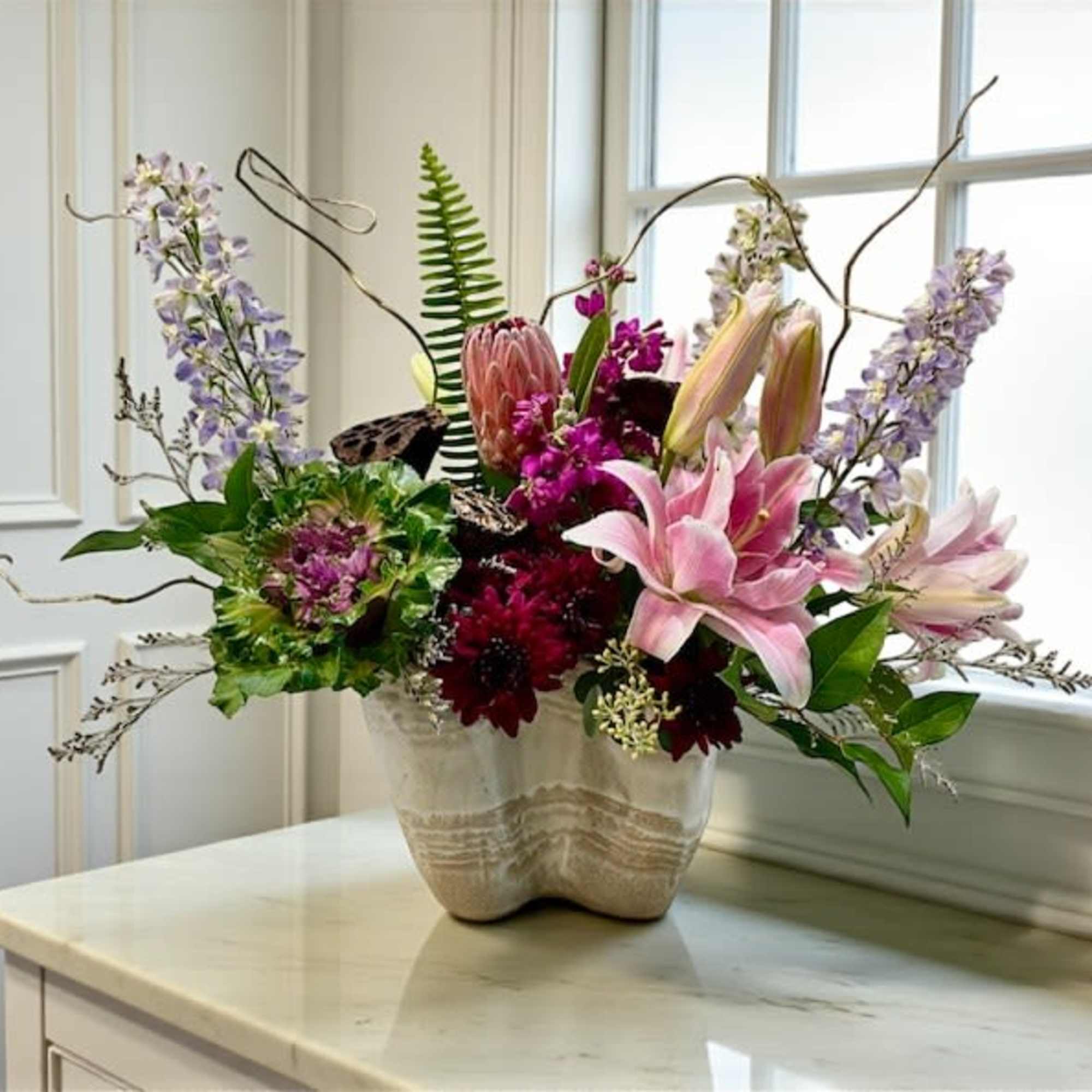 Mixed floral arrangement in a ceramic vase with pink lilies and purple blooms