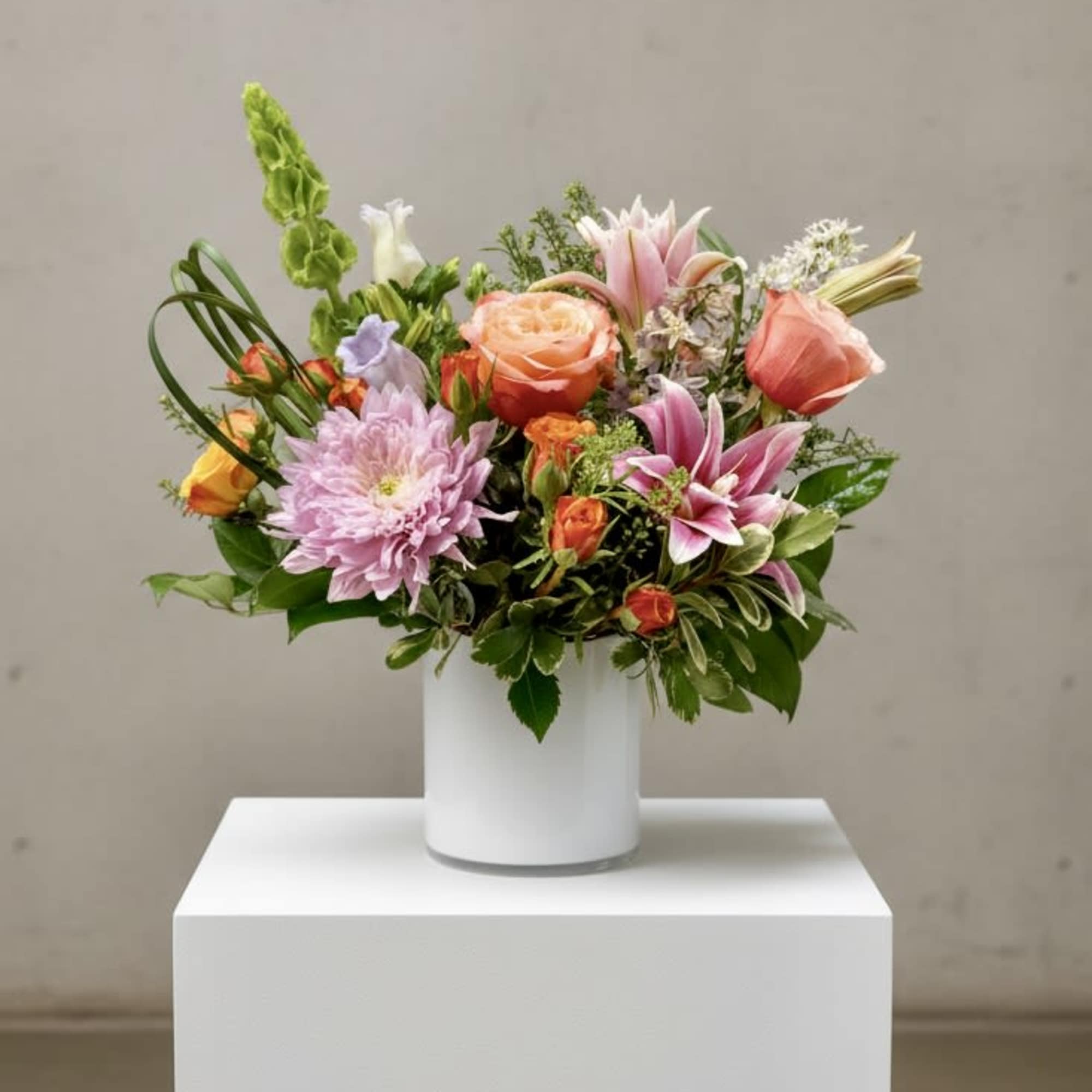 Mixed bouquet of pink, peach, and lavender flowers in a white vase