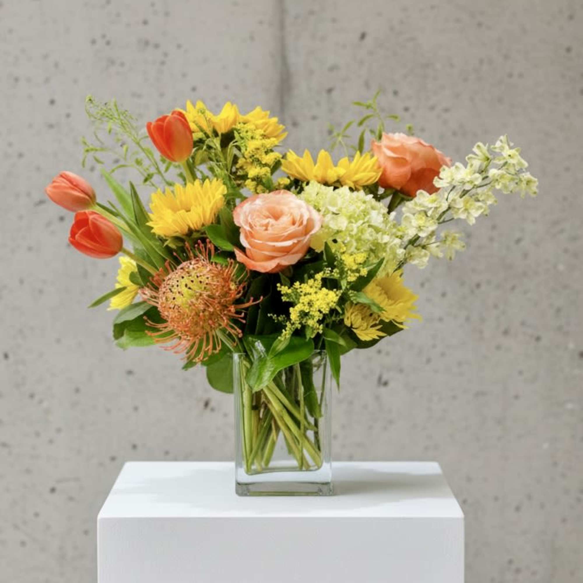 Mixed bouquet in a clear glass vase with orange, yellow, and peach flowers