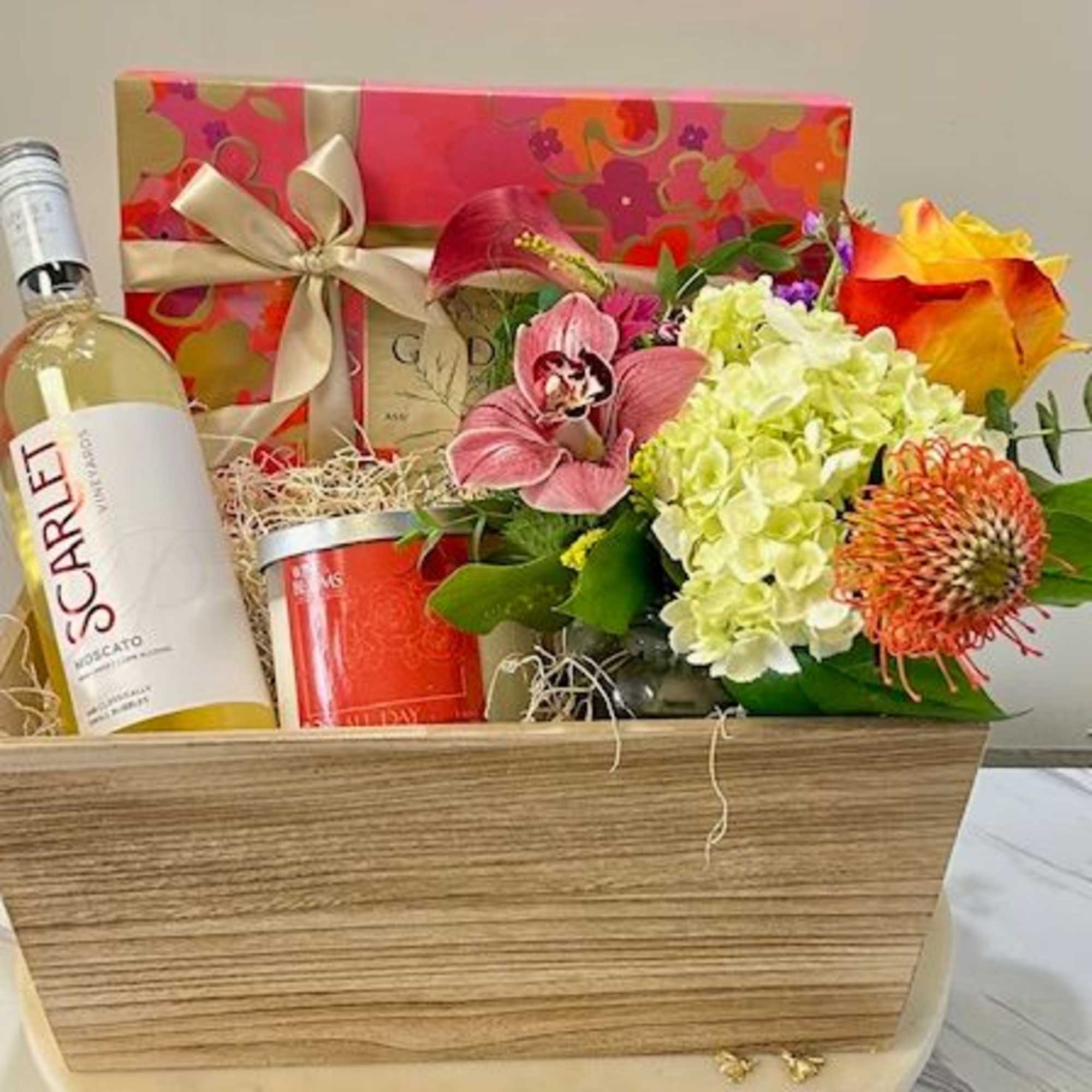 Gift basket with wine, flowers, and a candle in a wooden box