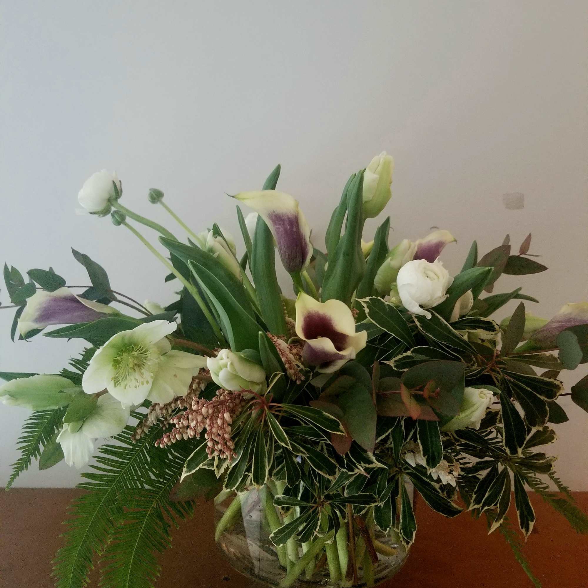 Low arrangement of white and purple calla lilies and white blooms in a clear glass pedestal bowl