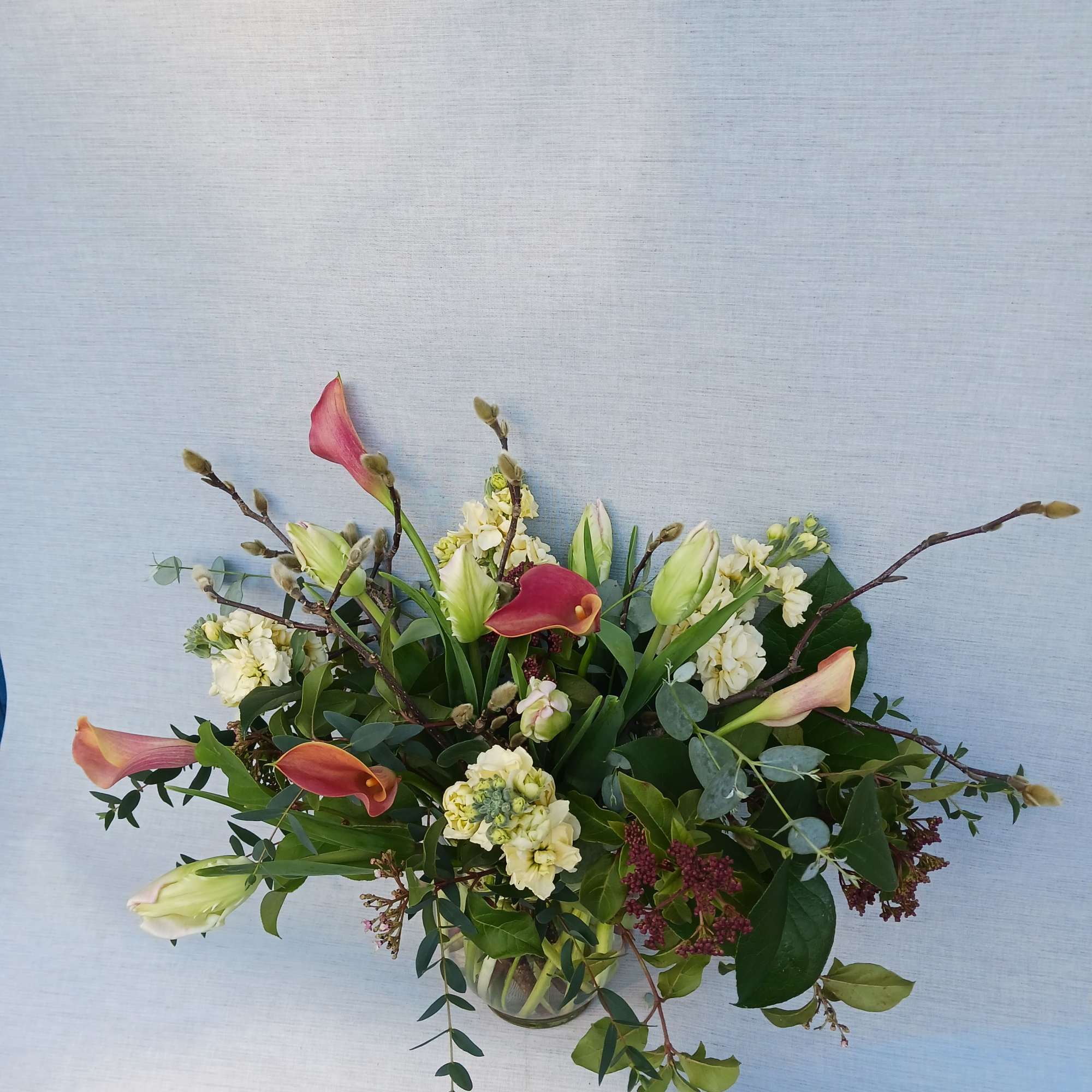 Low arrangement with peach calla lilies and cream flowers in a clear glass vase