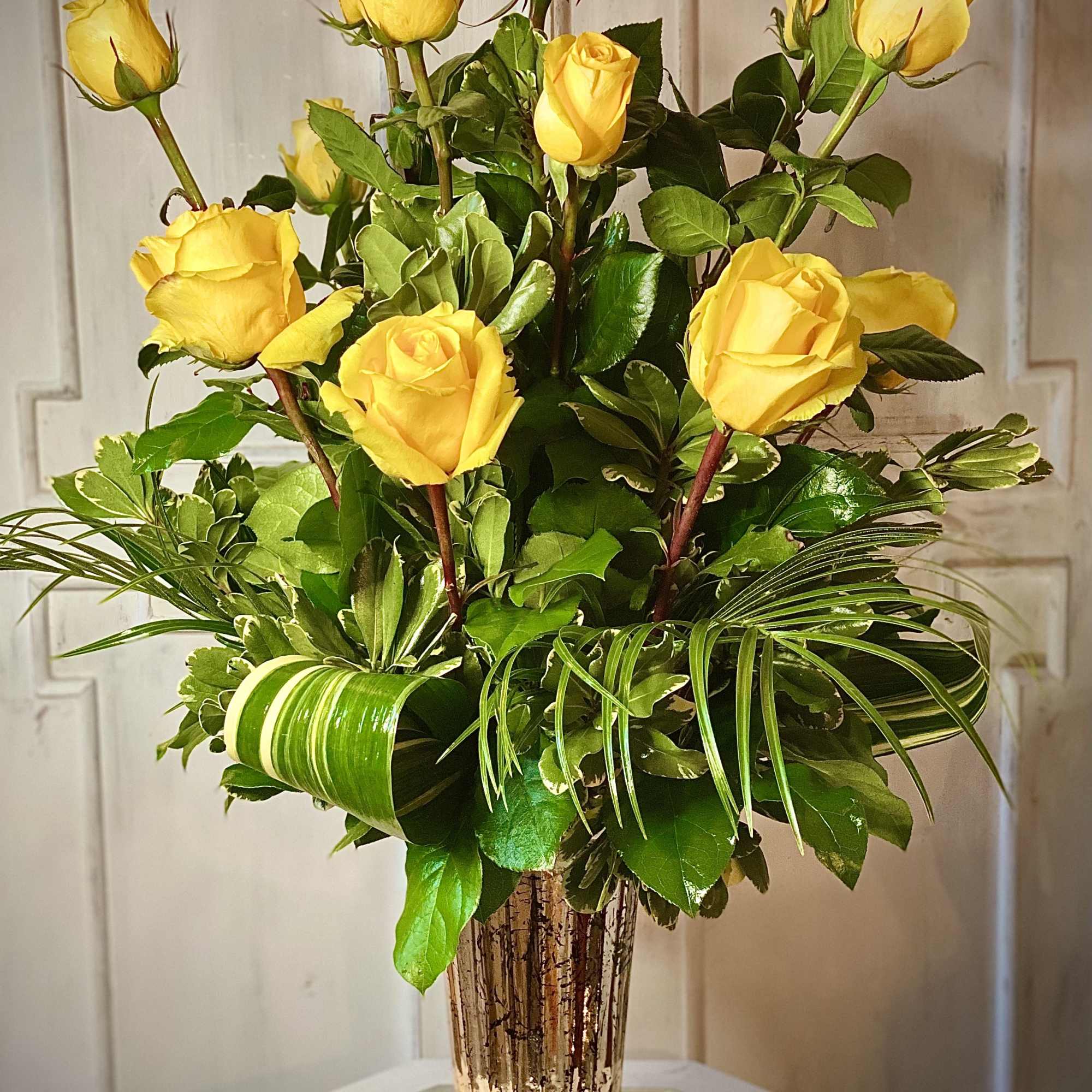 Yellow roses arranged in a tall clear vase with lush greenery