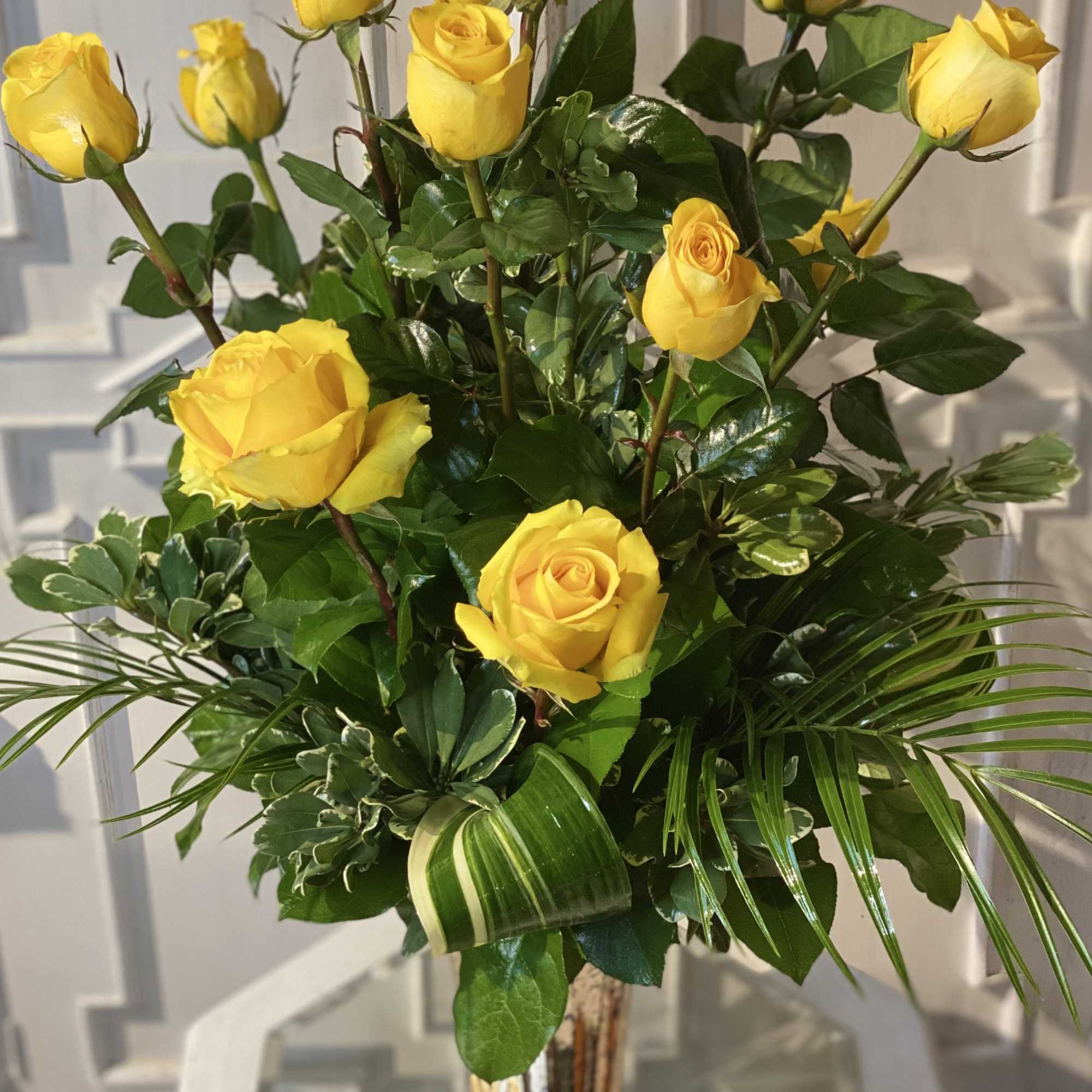 Yellow roses arranged in a clear glass vase with glossy greenery