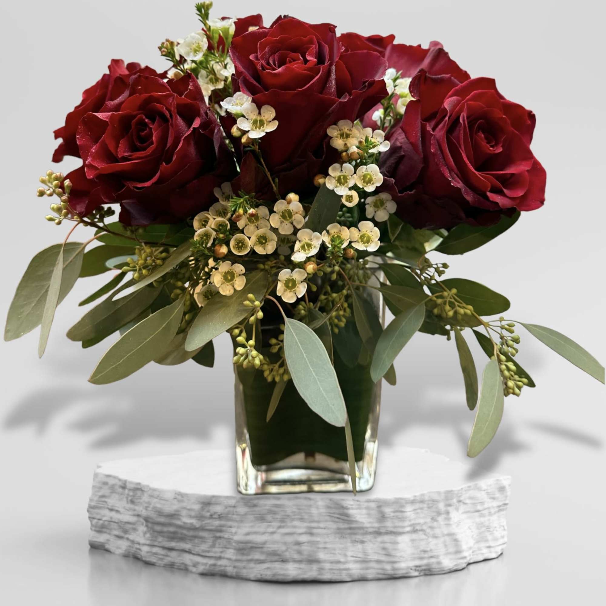 Red roses in a glass vase with small white filler flowers