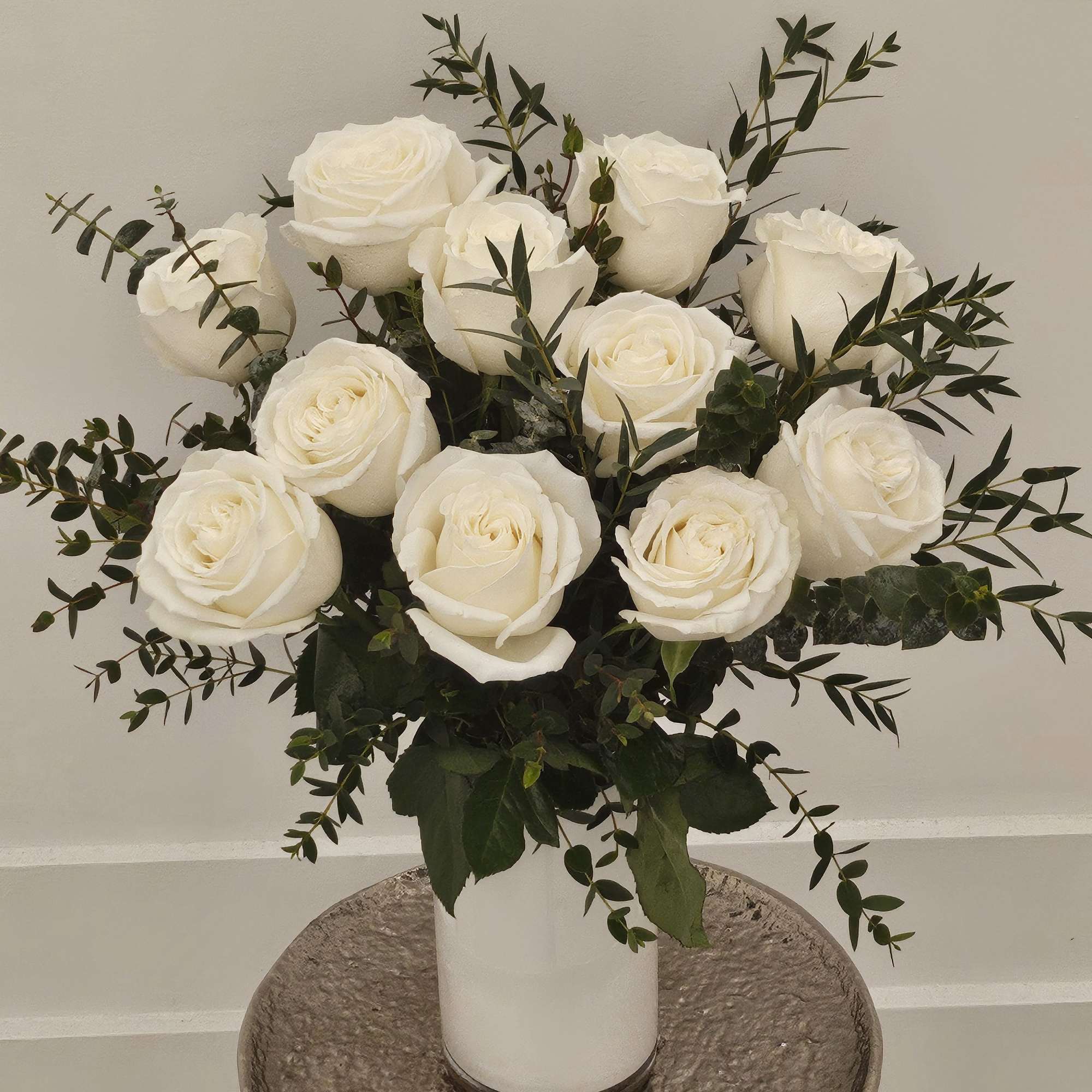 White roses arranged in a white vase with dark greenery