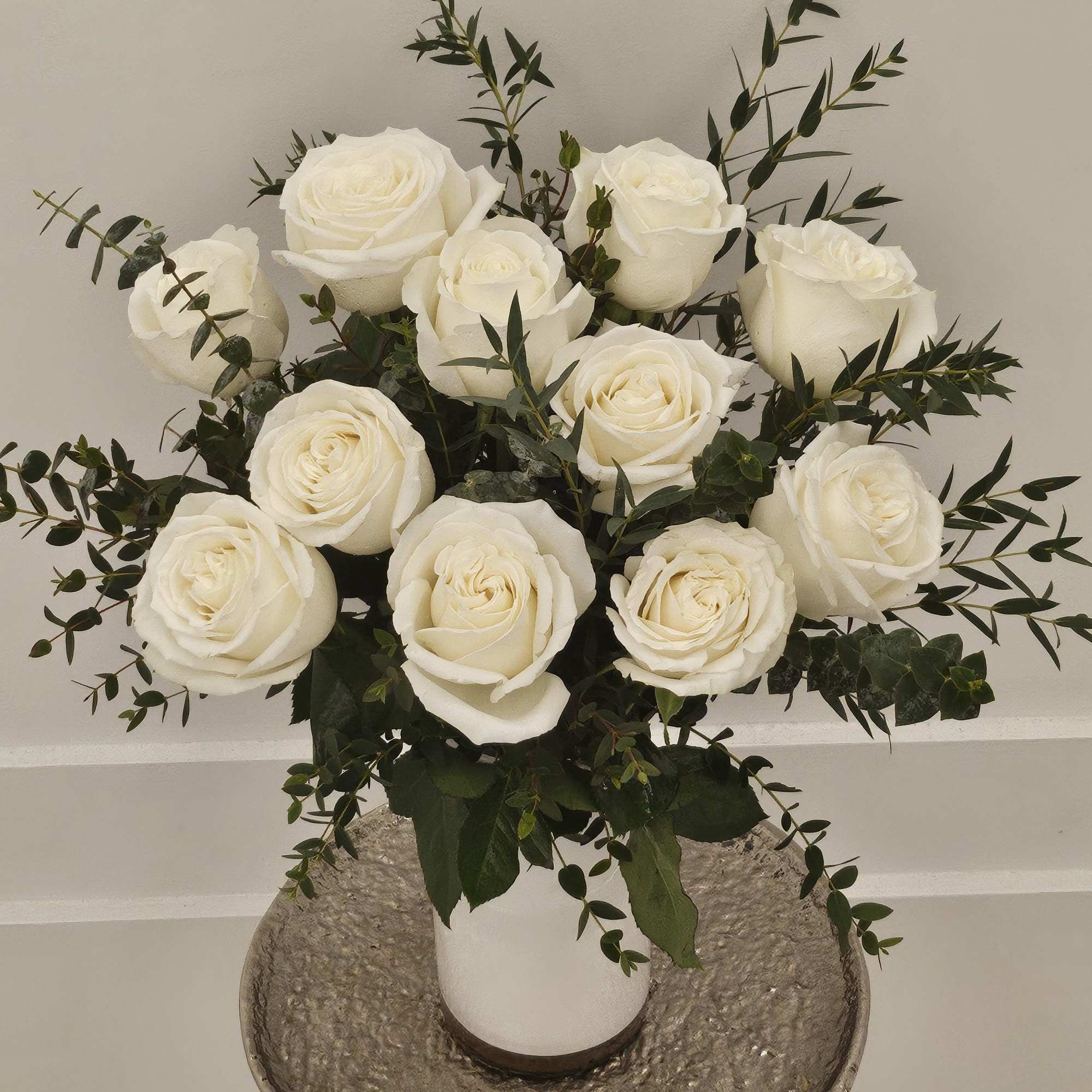 White roses arranged in a white vase with dark greenery