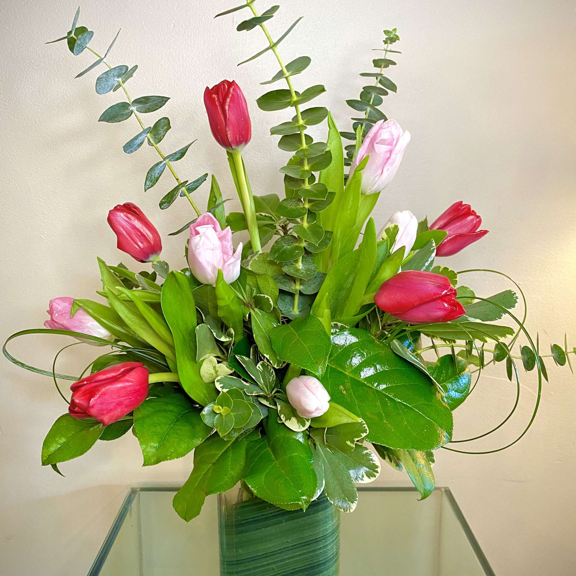 Pink and red tulips in a glass vase with tall eucalyptus stems