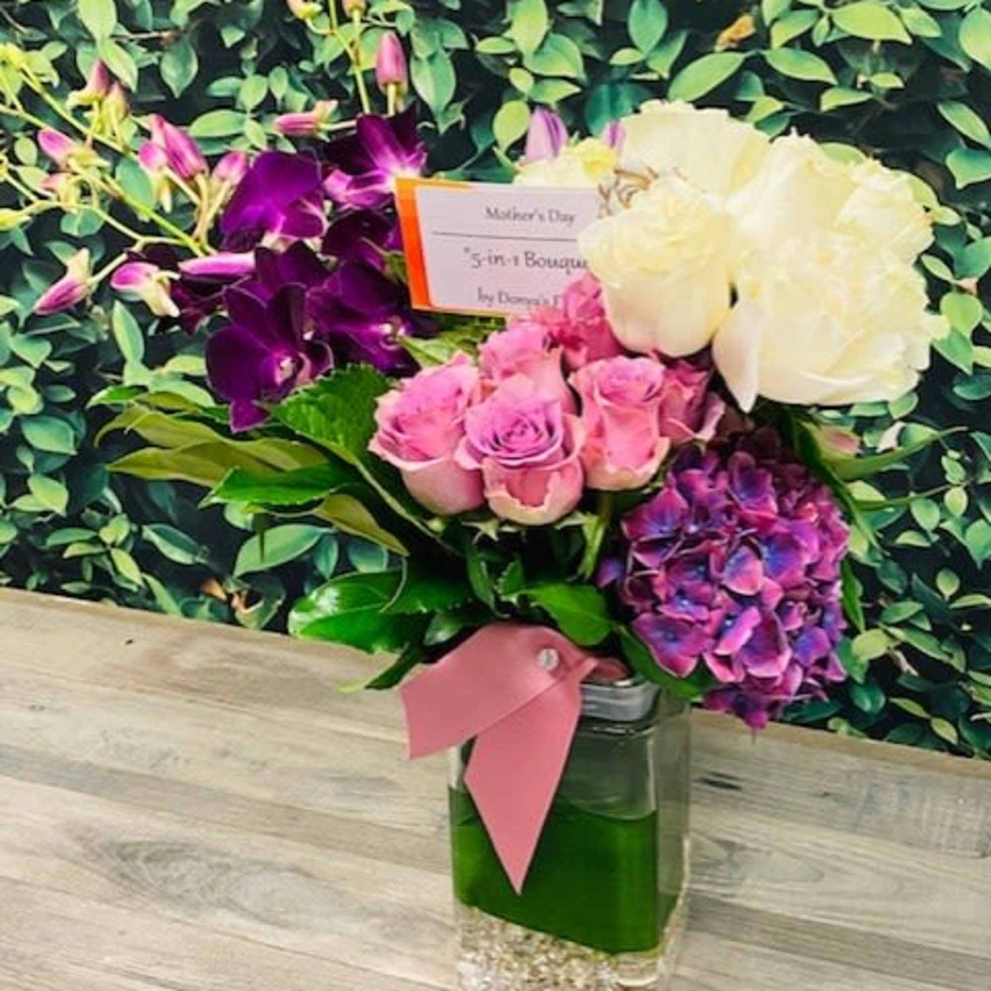 Bouquet of pink roses, white roses, purple orchids, and hydrangea in a glass vase
