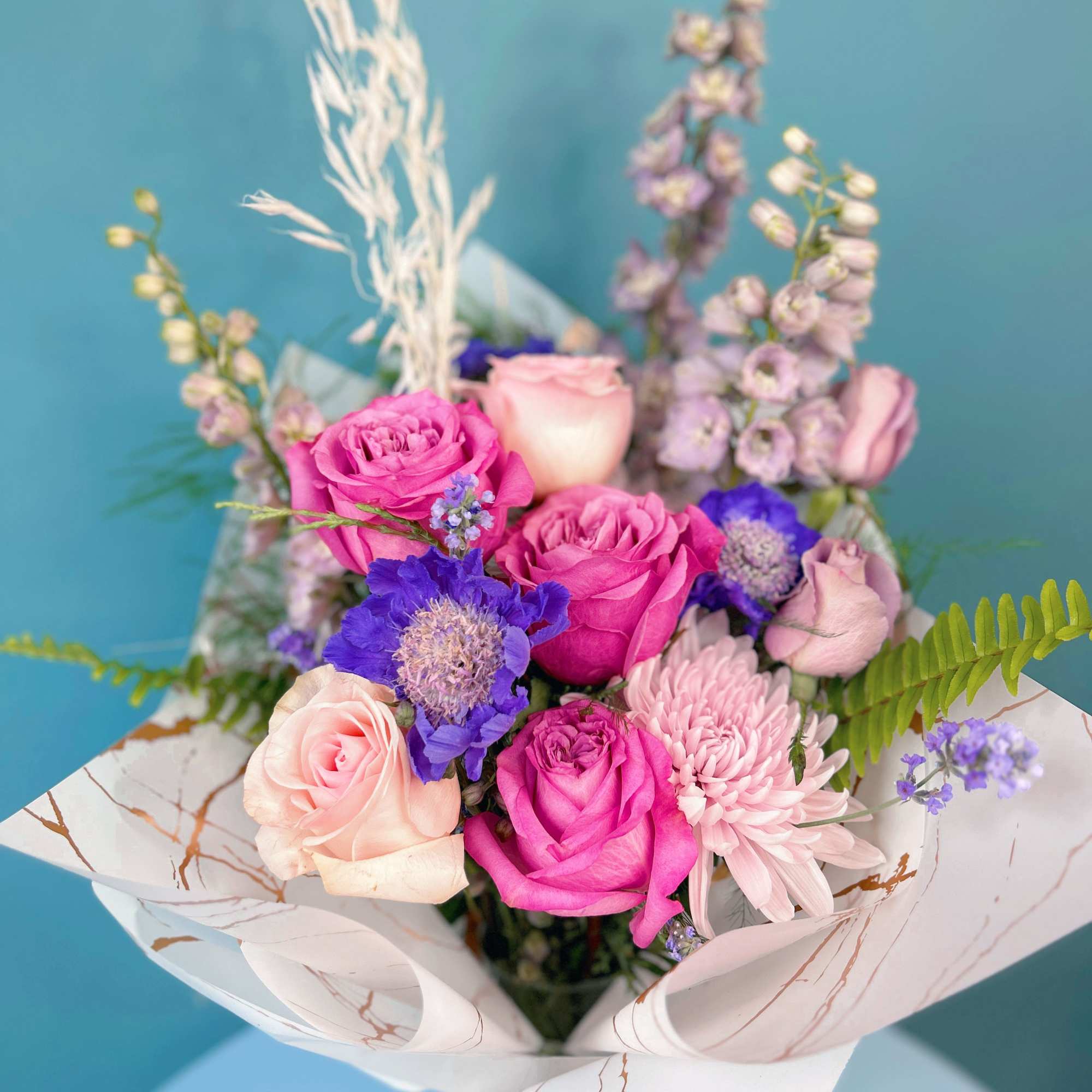 Bouquet of pink and purple roses with a pale chrysanthemum in white wrap