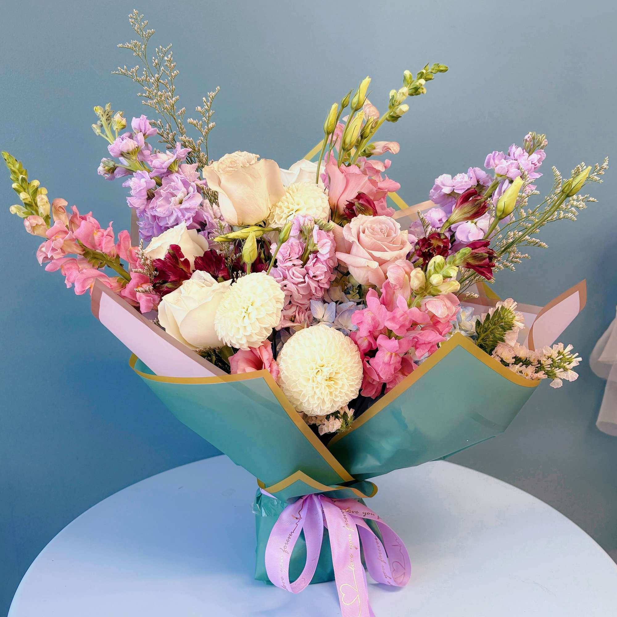 Pastel bouquet of pink, cream, and lavender flowers wrapped in teal paper