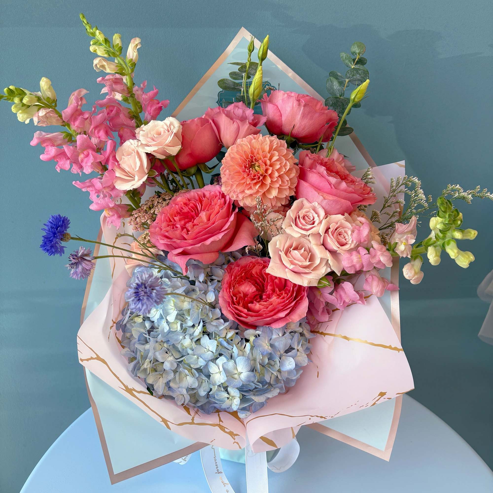Bouquet of pink roses, hydrangea, and snapdragons in pastel wrapping