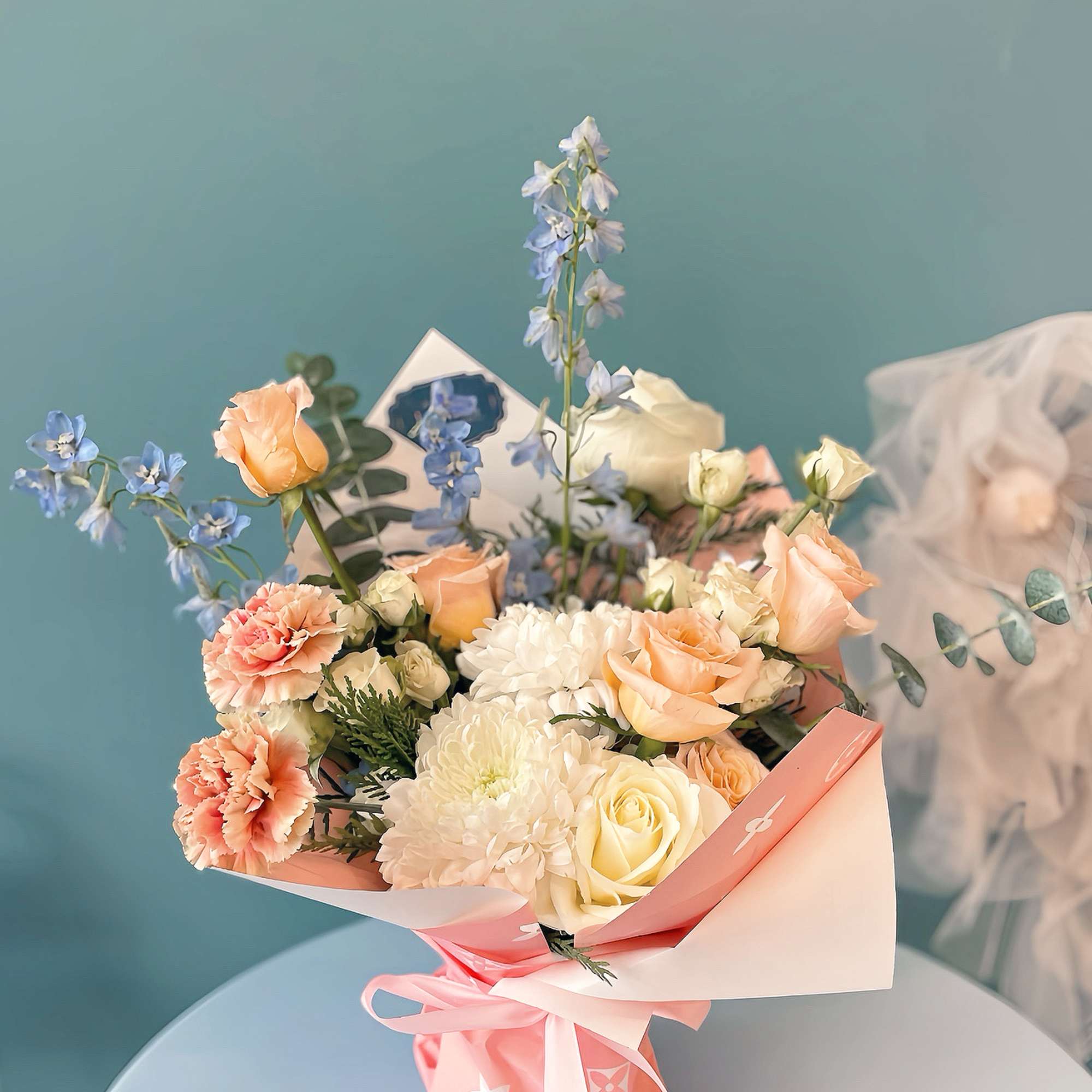 Bouquet of peach and white flowers with blue accents in pink wrapping