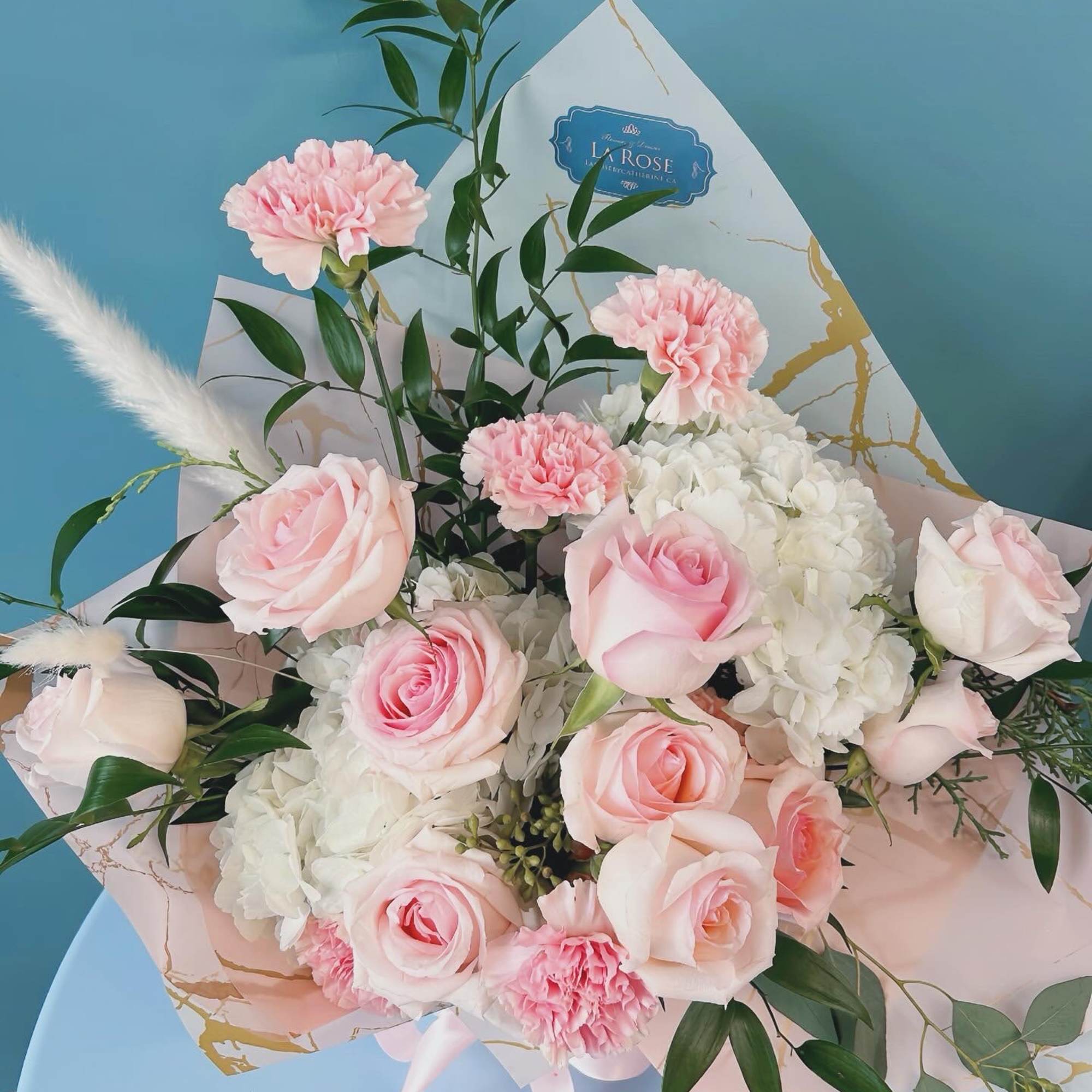 Pink roses and carnations arranged with white hydrangeas in pastel wrapping
