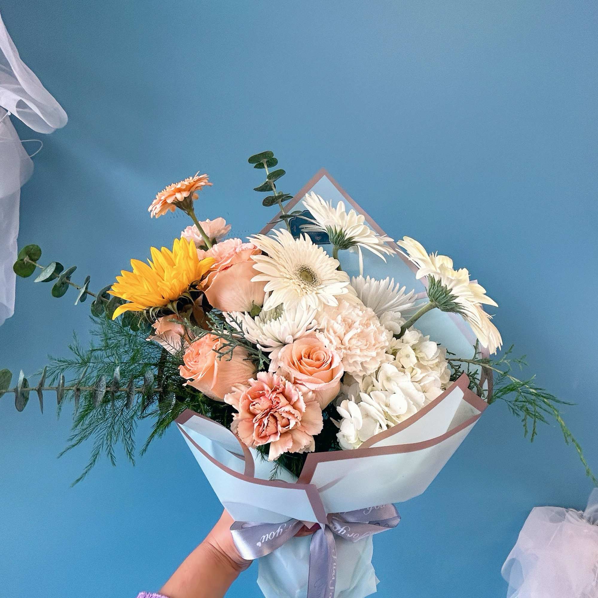 Handheld bouquet of peach, white, and yellow flowers wrapped in paper