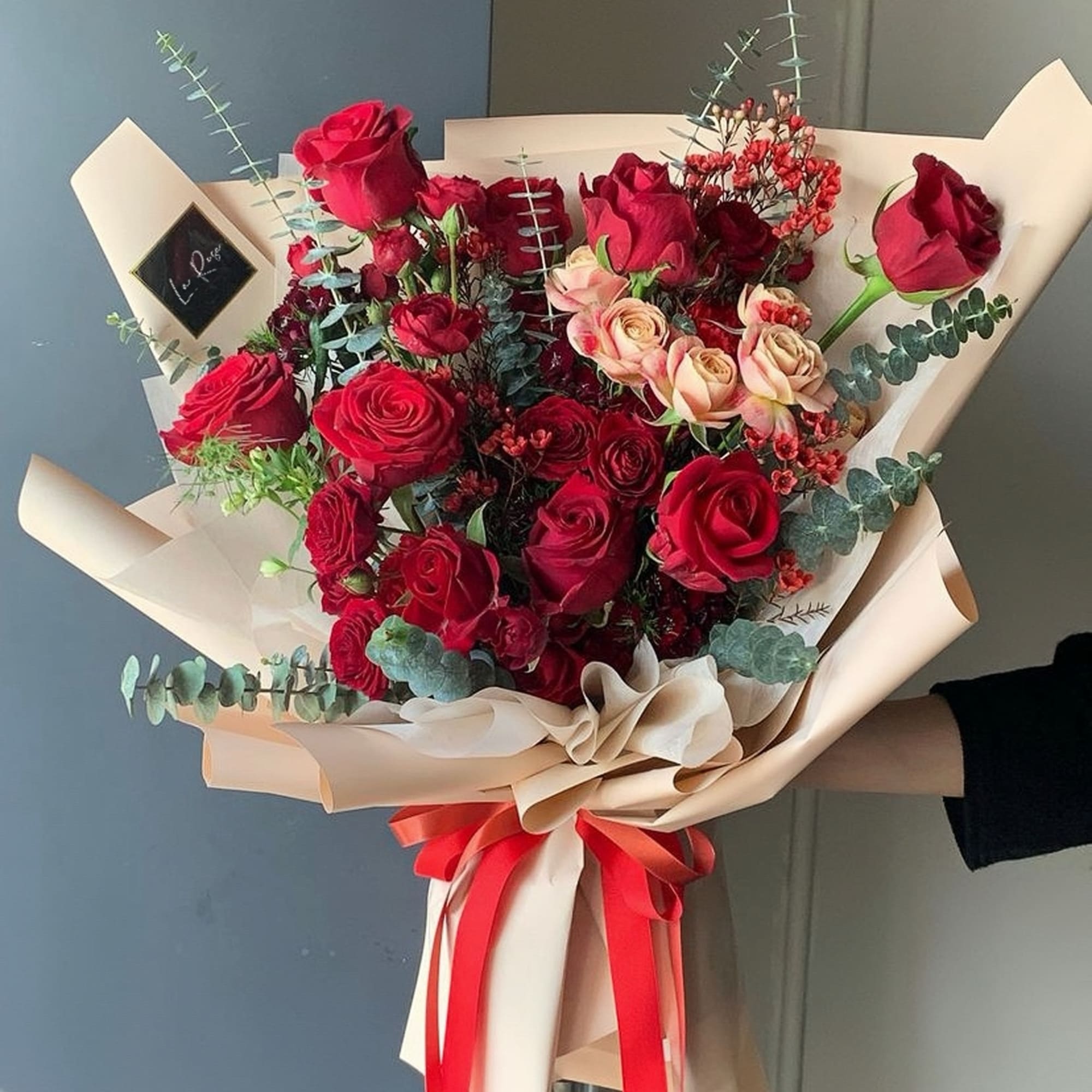 Bouquet of red and blush roses wrapped in beige paper with a red ribbon