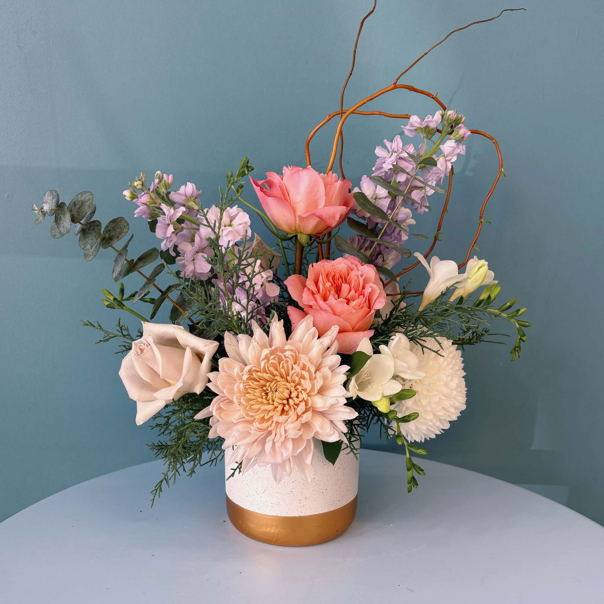 Mixed pastel floral arrangement in a white and gold vase