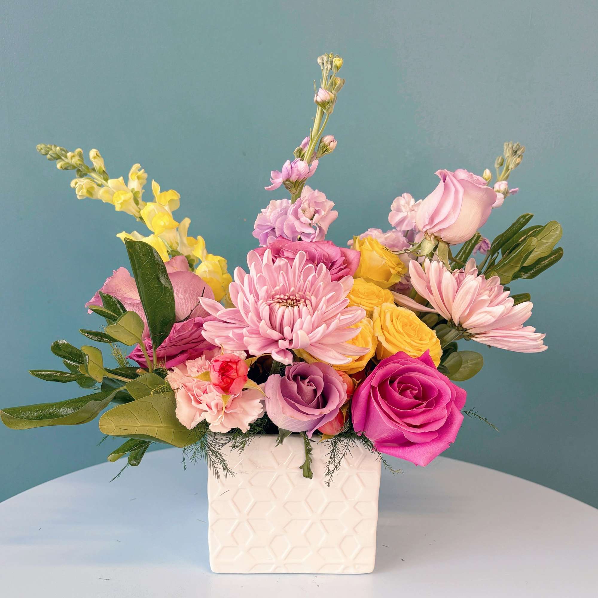 Pink and yellow mixed flower arrangement in a white square vase