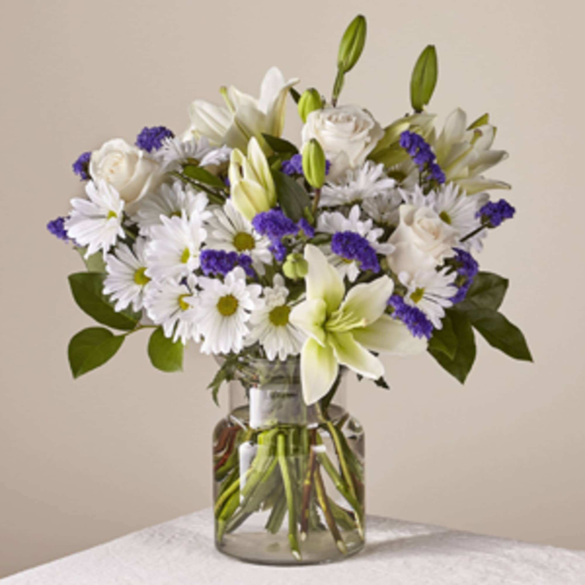 White lilies, roses, and daisies in a clear glass vase