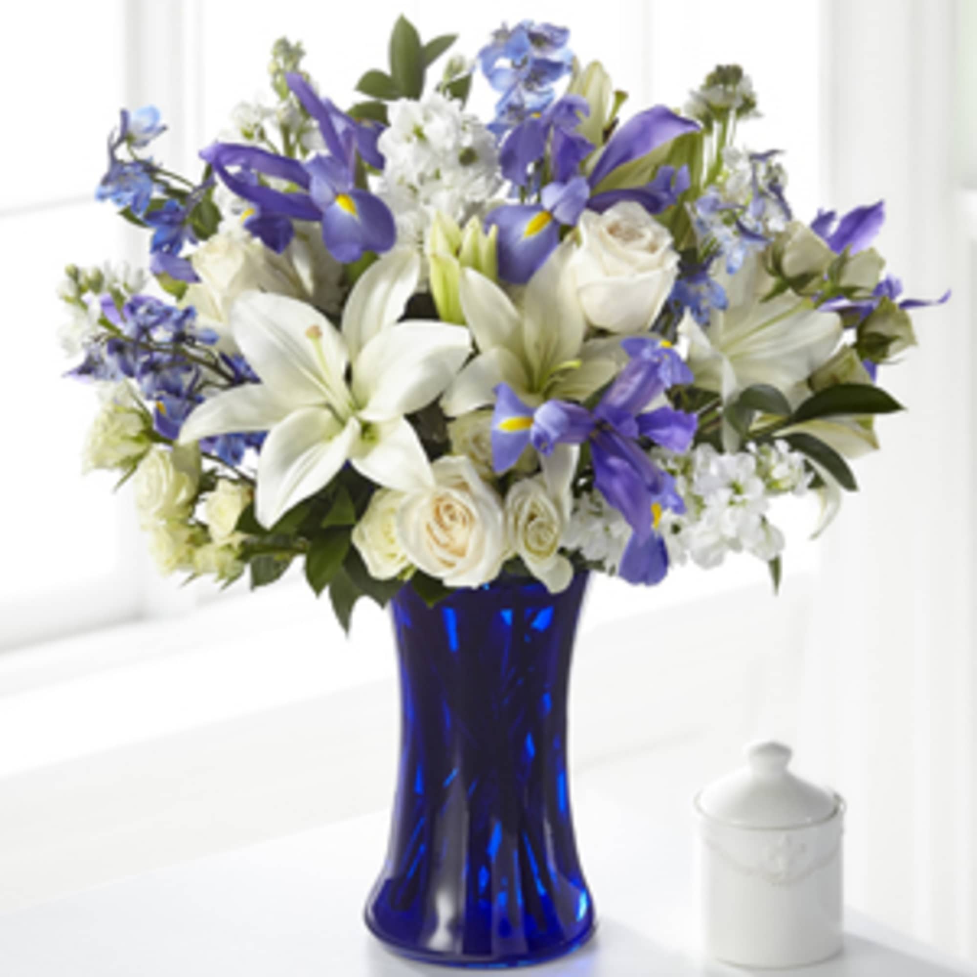 White lilies, roses, and blue irises arranged in a cobalt blue glass vase