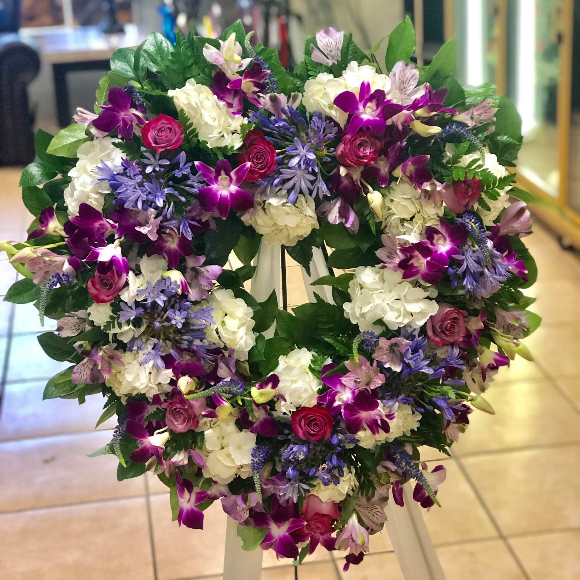 Heart-shaped standing wreath with purple orchids, pink roses, and white hydrangeas on a white easel