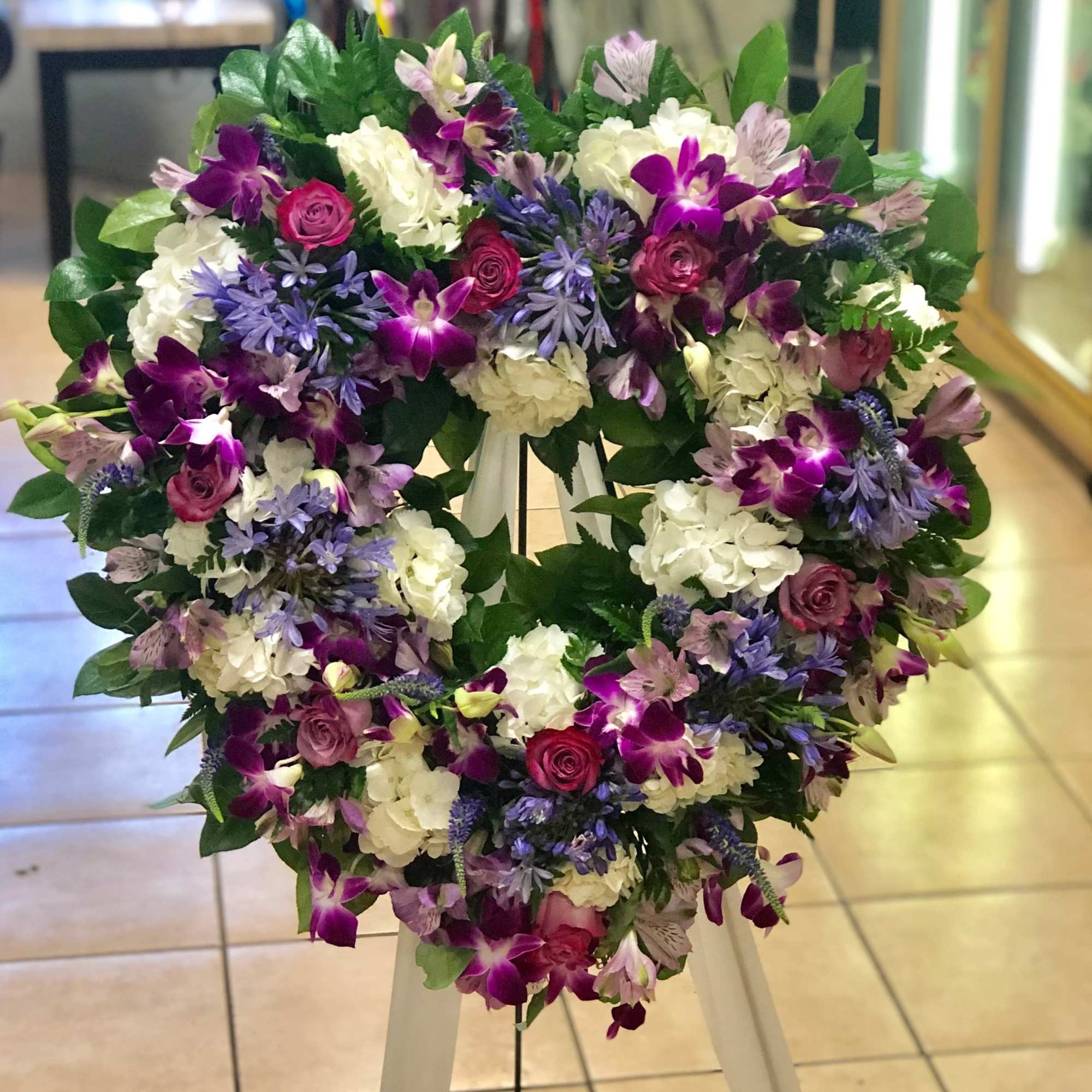 Heart-shaped standing wreath with purple, pink, and white flowers on an easel