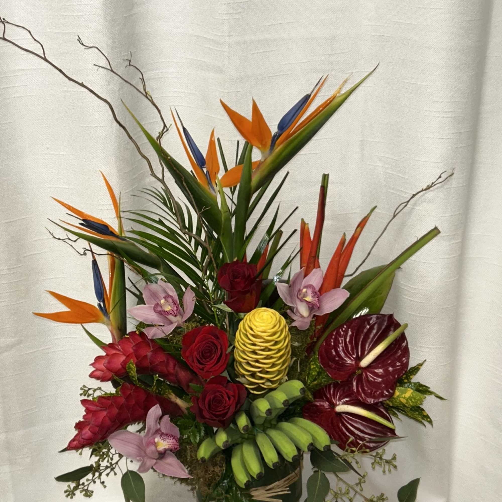 Tropical bouquet with orchids, roses, anthuriums, and bird of paradise in a glass vase