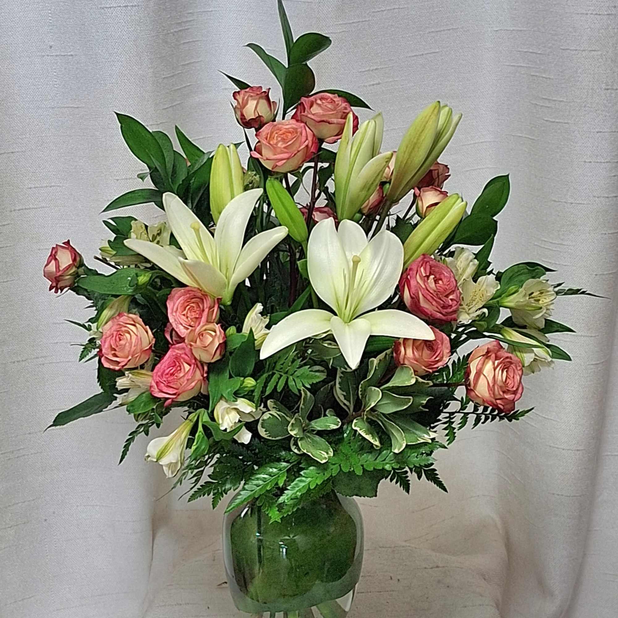 Mixed bouquet of white lilies and pink roses arranged in a clear glass vase