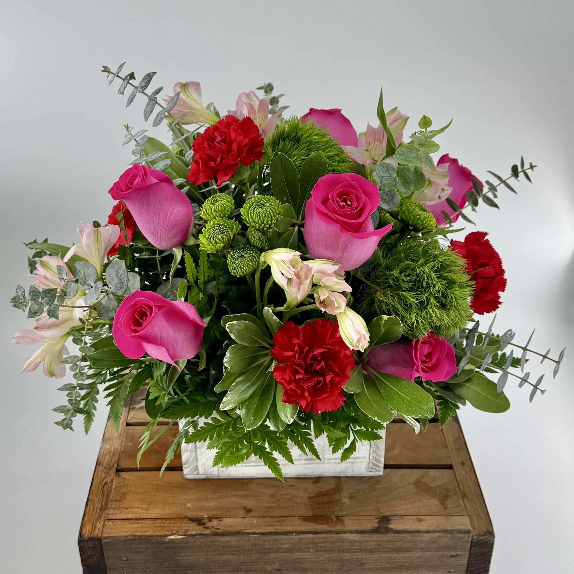 Bright arrangement of hot pink roses, red carnations, and green accents in a white box container