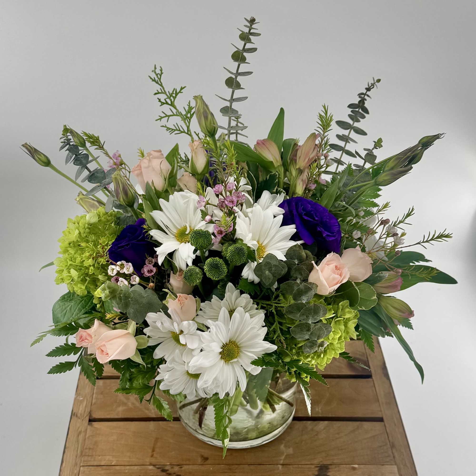 Mixed bouquet of white daisies, green hydrangeas, peach roses and purple blooms in a clear glass vase