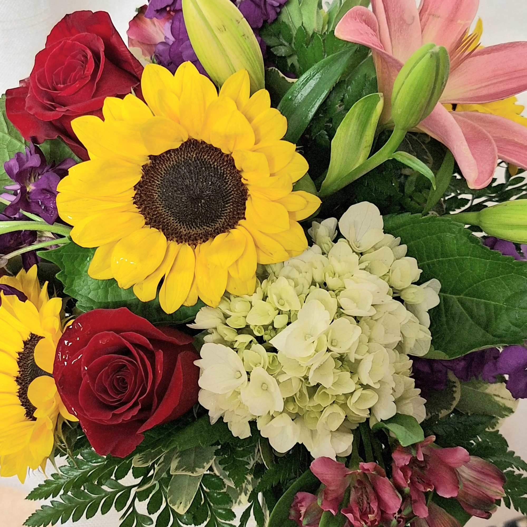Mixed bouquet with yellow sunflowers, red rose, white hydrangea, pink lily and other blooms.