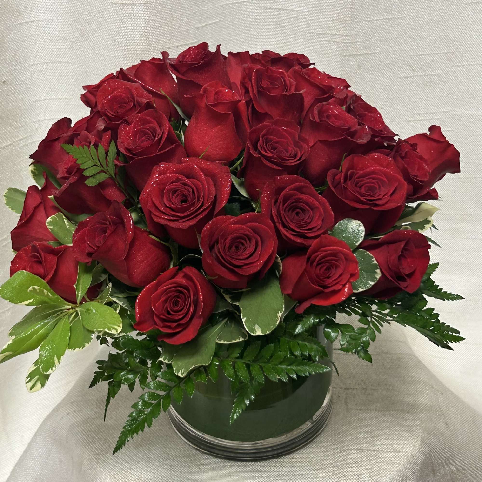 Low round arrangement of red roses in a clear glass cylinder vase with foliage