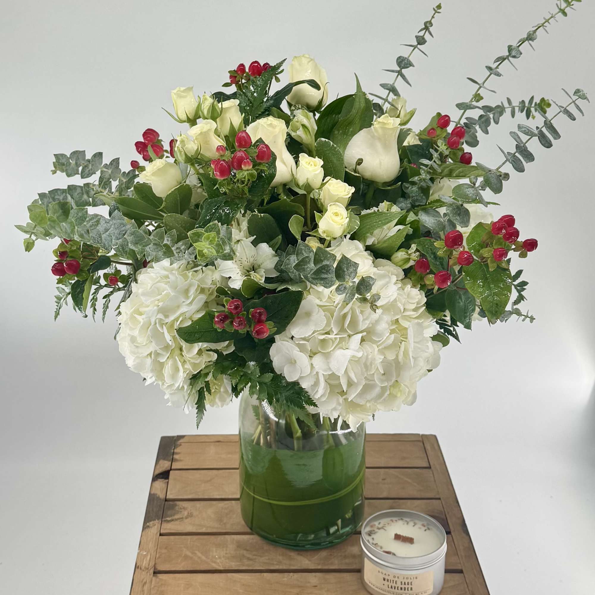 White floral arrangement in a glass vase with red berry accents