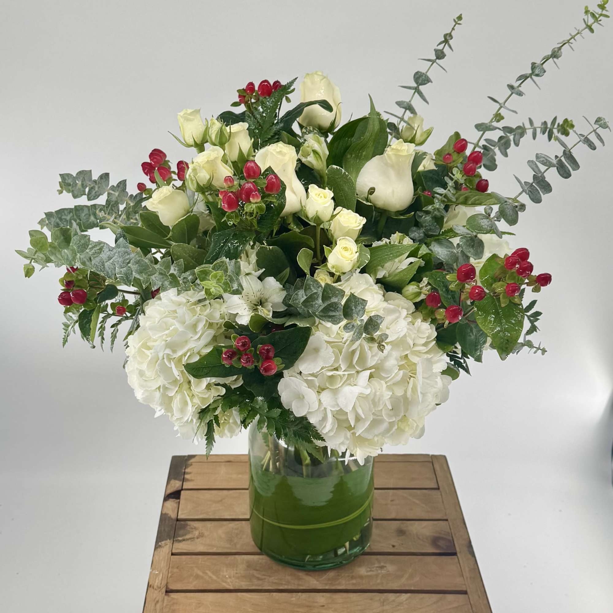 White roses and hydrangeas in a green glass vase with red berry accents