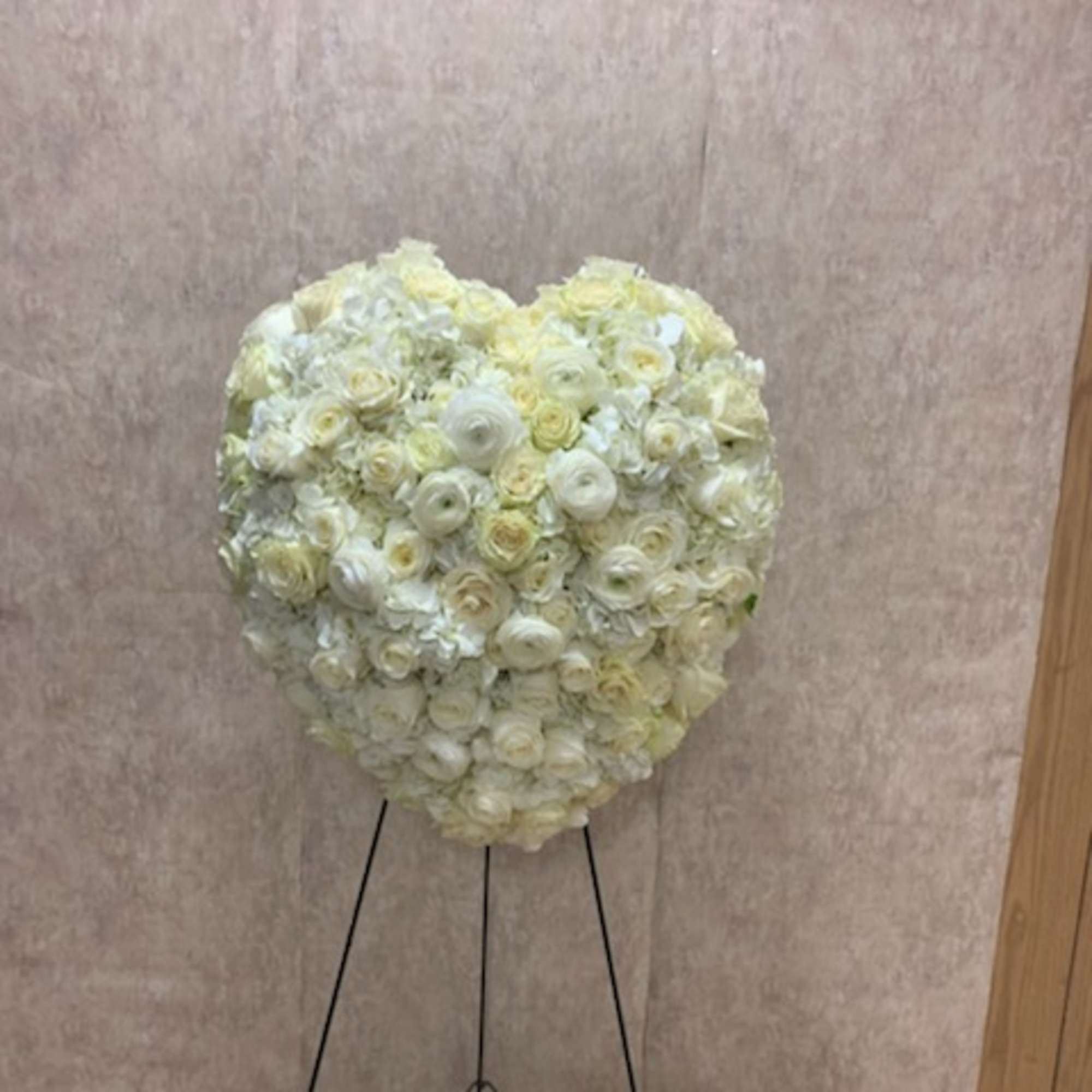 Heart-shaped arrangement of white and cream roses on a tall black easel stand
