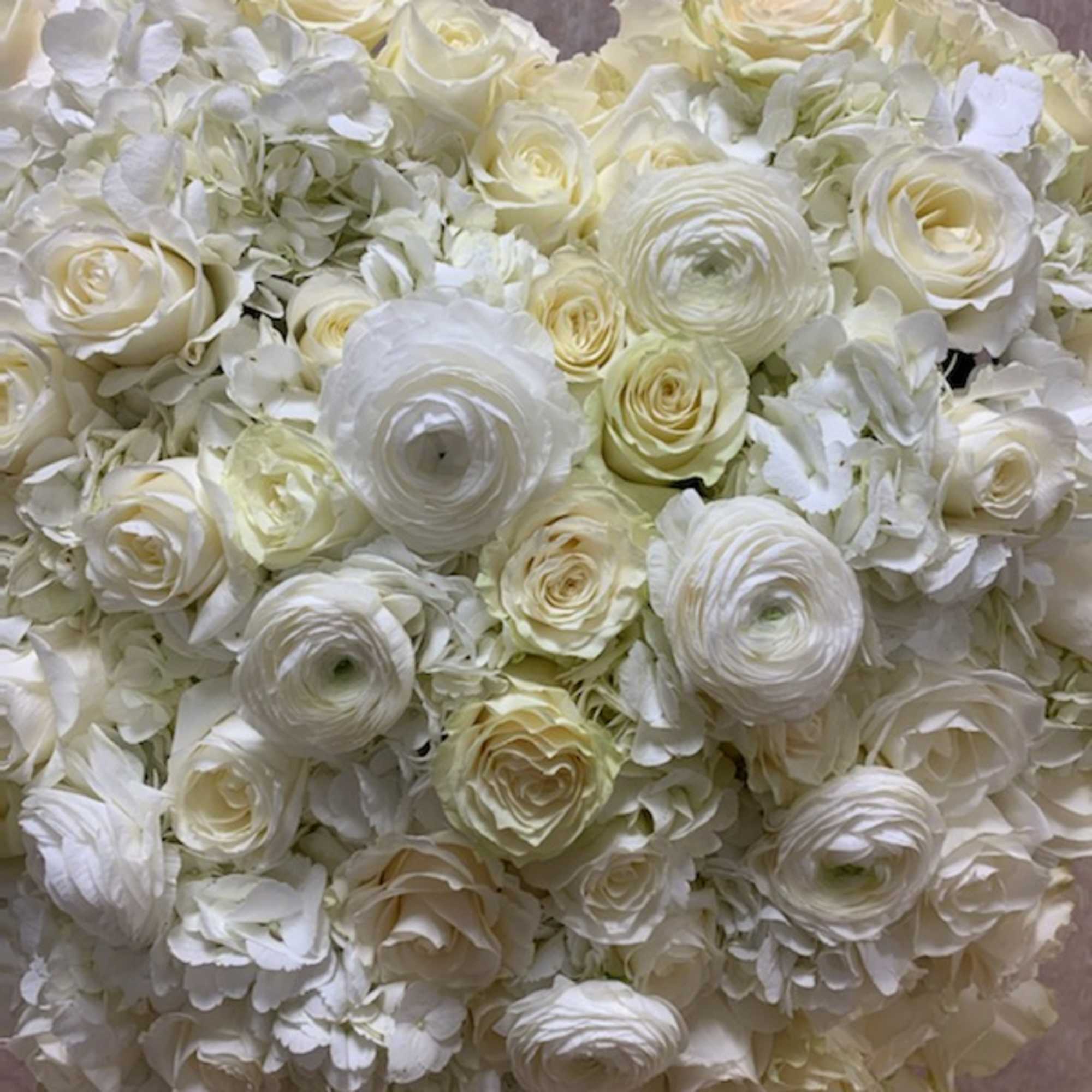 Heart-shaped arrangement of white and ivory roses, ranunculus, and hydrangeas.