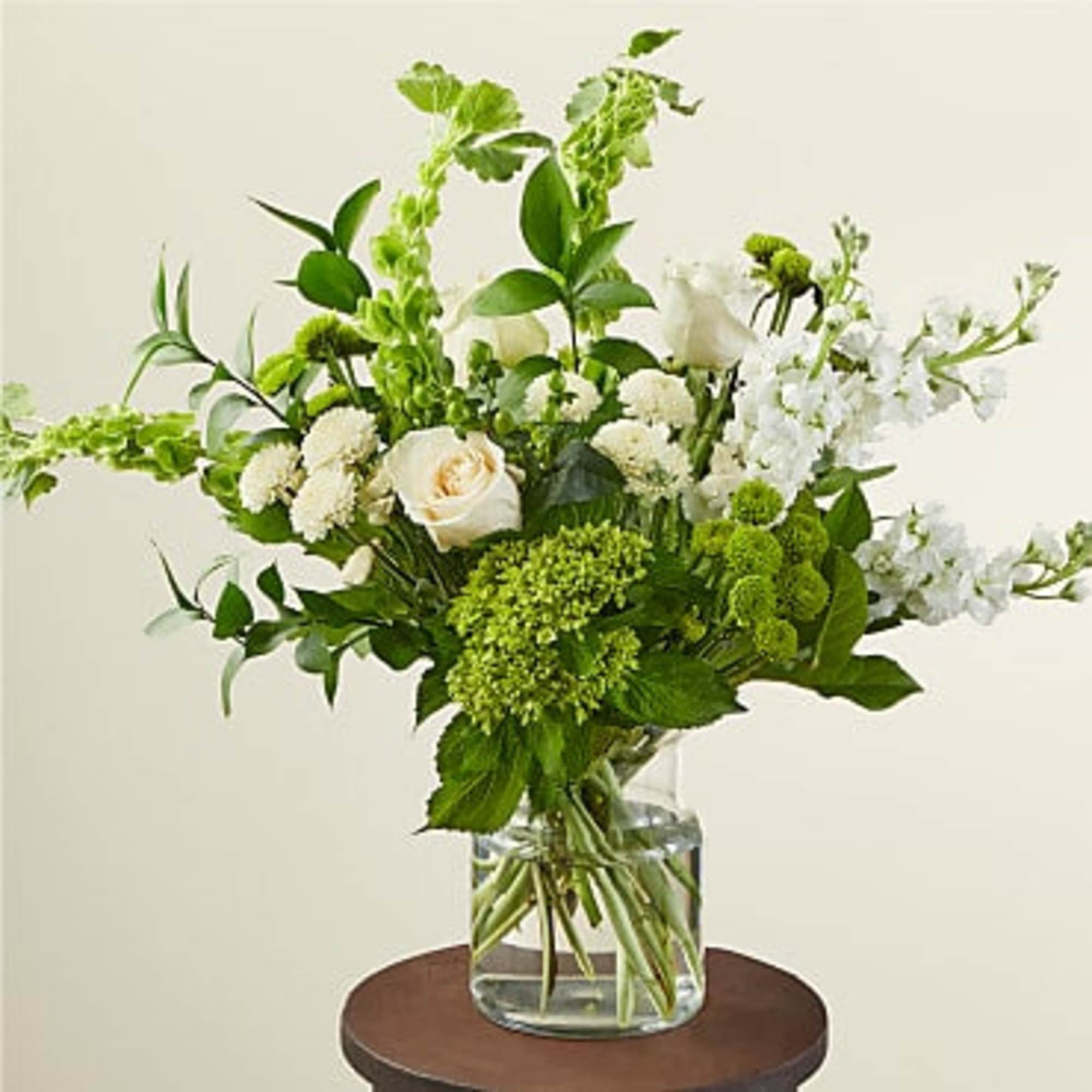 Arrangement of white and green flowers including roses and mums in a clear glass vase