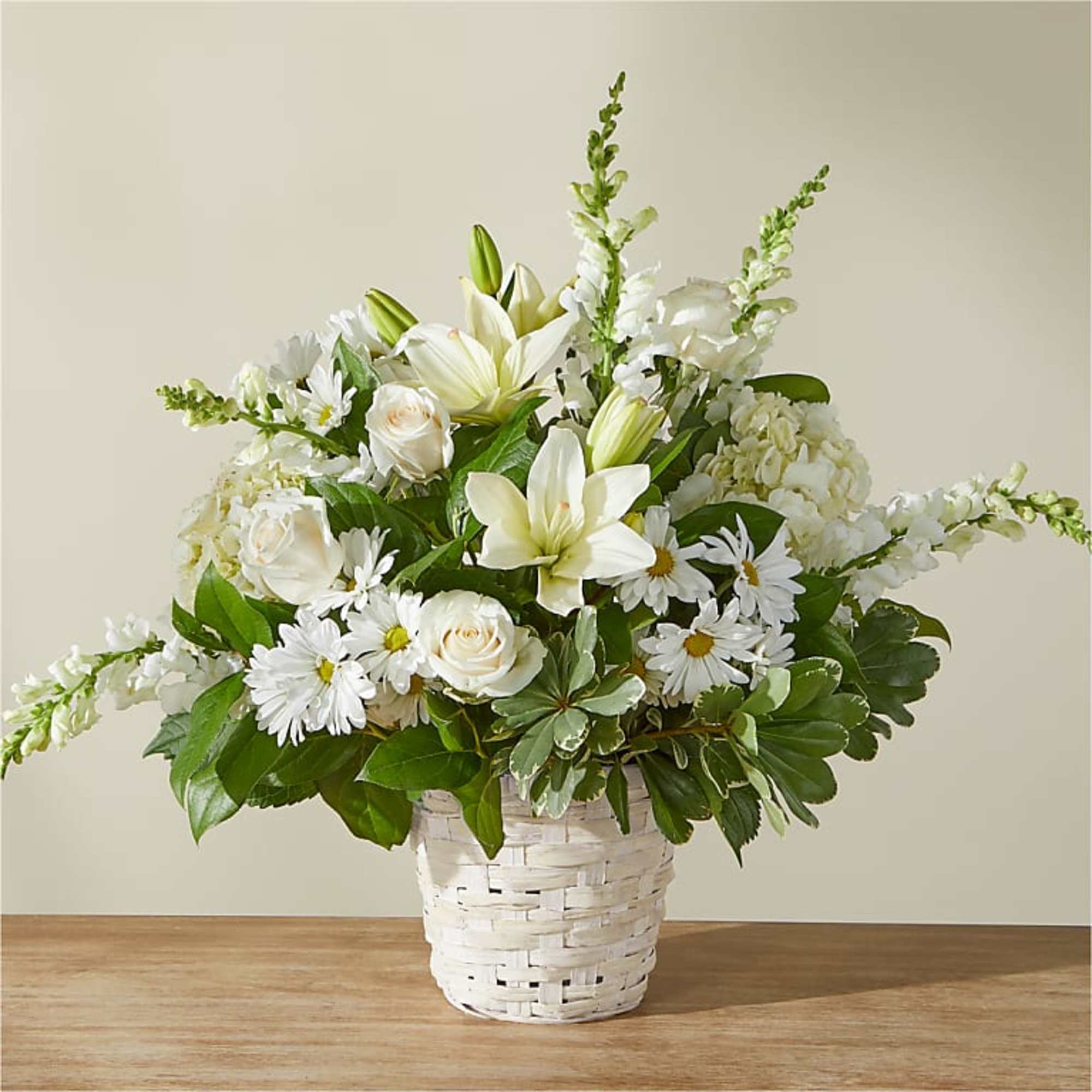 White lilies, roses, daisies, and snapdragons arranged in a white woven basket
