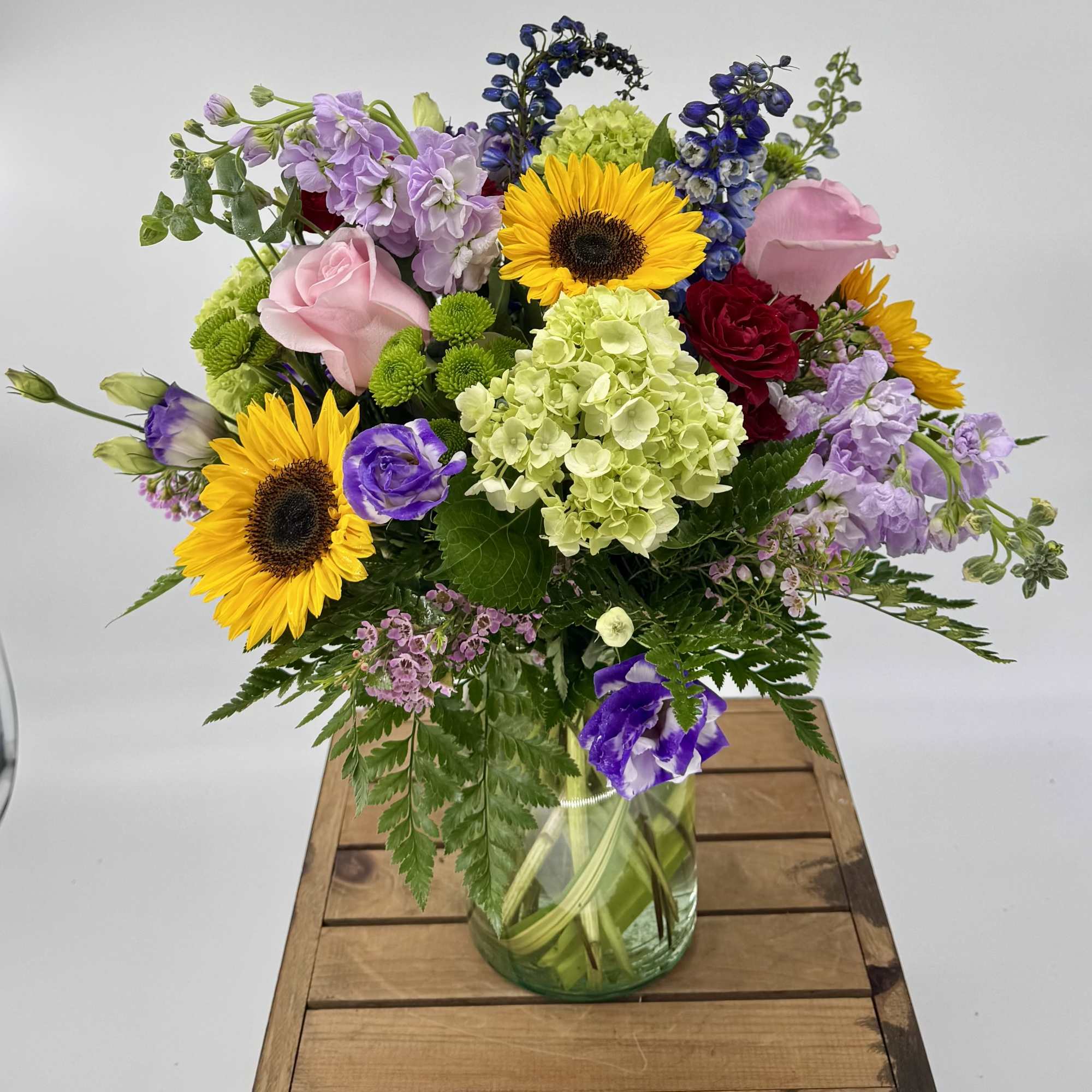 Mixed bouquet with sunflowers, pink roses, and green hydrangea in a clear glass vase
