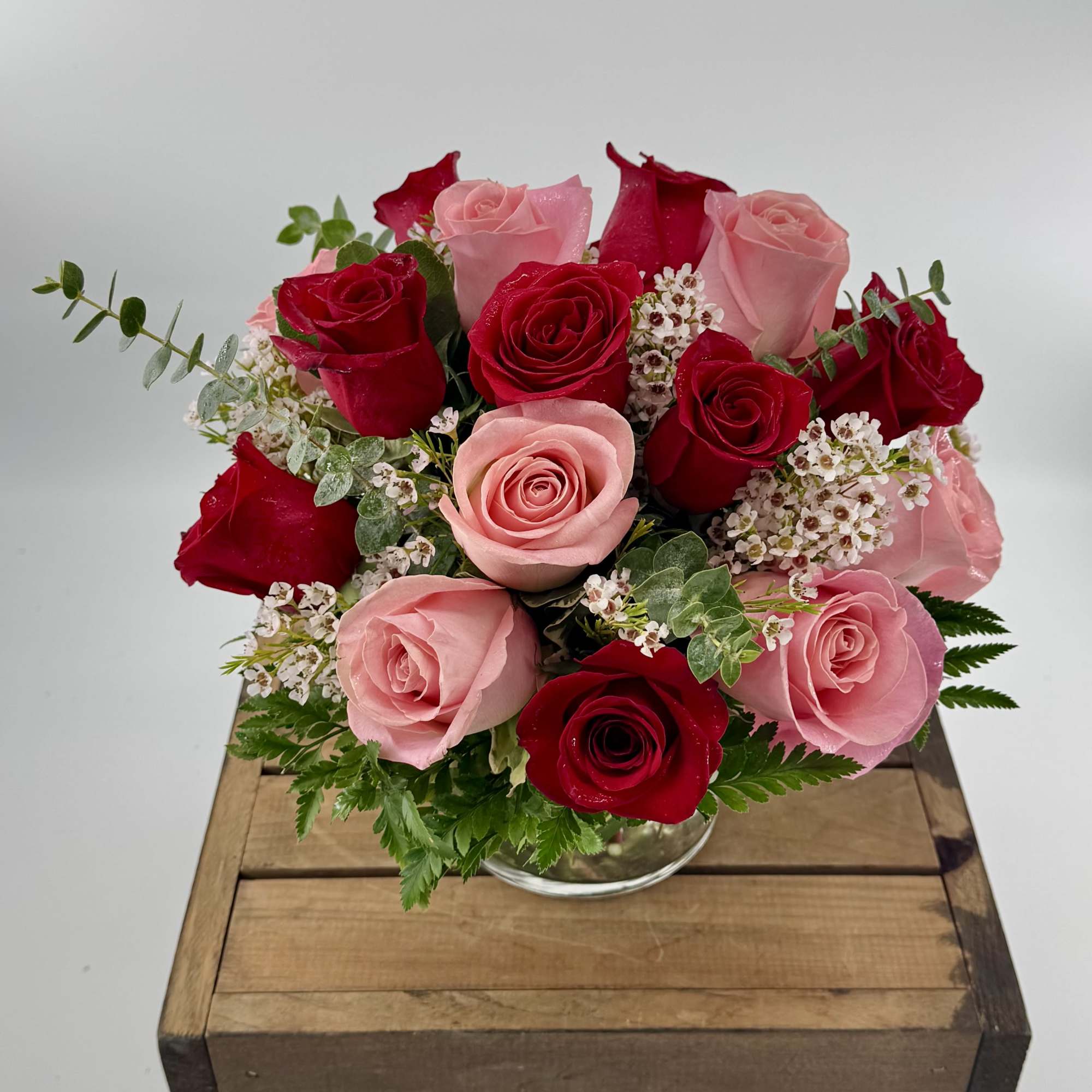 Round arrangement of red and pink roses with small white blooms in a clear glass vase