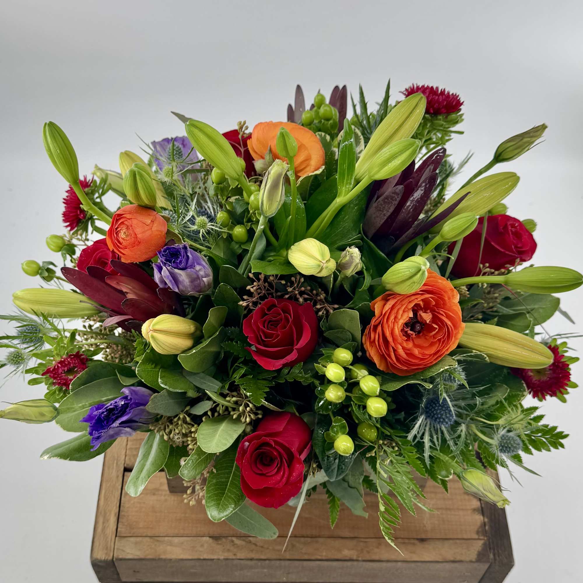 Mixed bouquet of red roses, orange ranunculus, and lilies in a wooden box