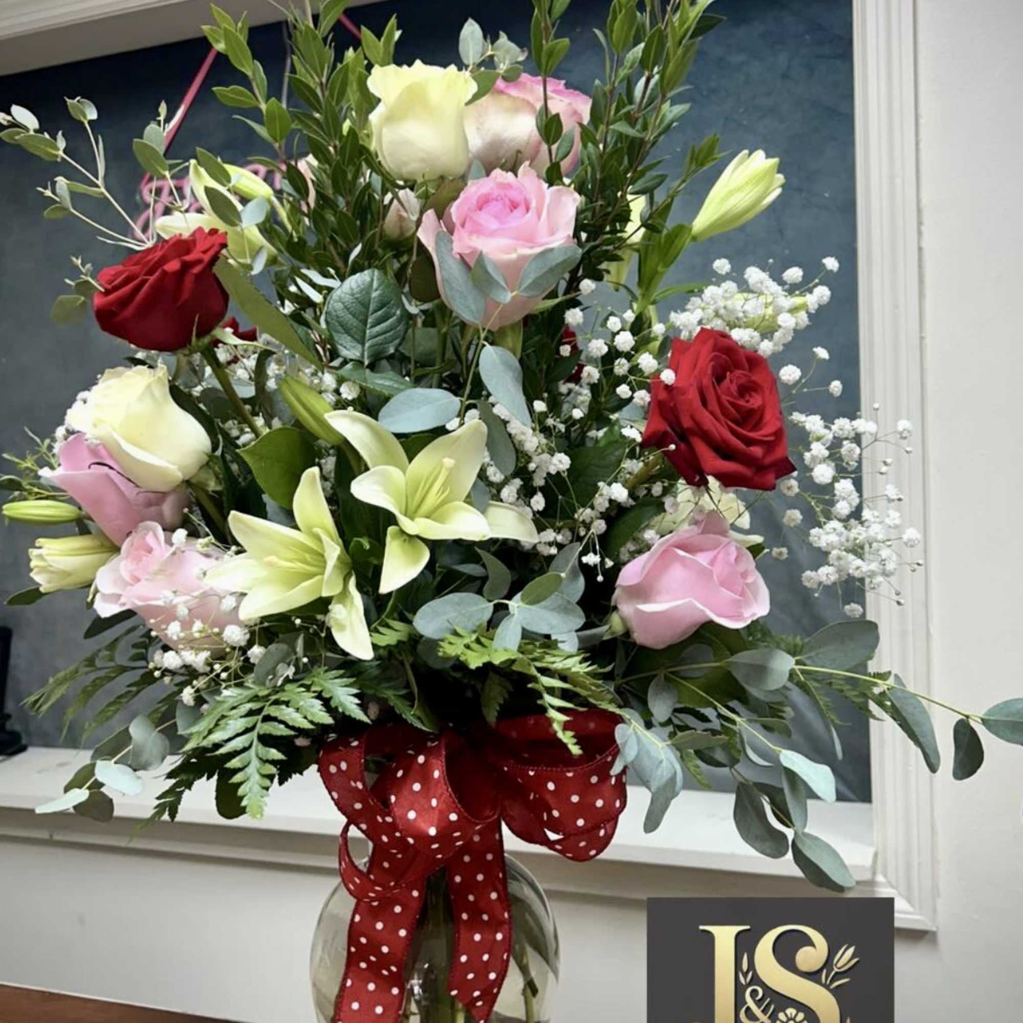 Mixed roses and lilies in a glass vase with a red polka-dot ribbon
